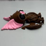 Left side of a figure of a brown bat with pink ears and nose on a gray background