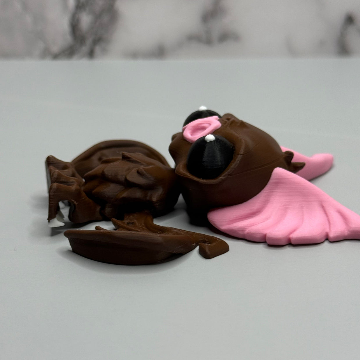 Right side of a figure of a brown bat with pink ears and nose on a gray background