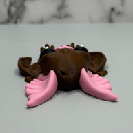 Top side of a figure of a brown bat with pink ears and nose on a gray and marble gray background