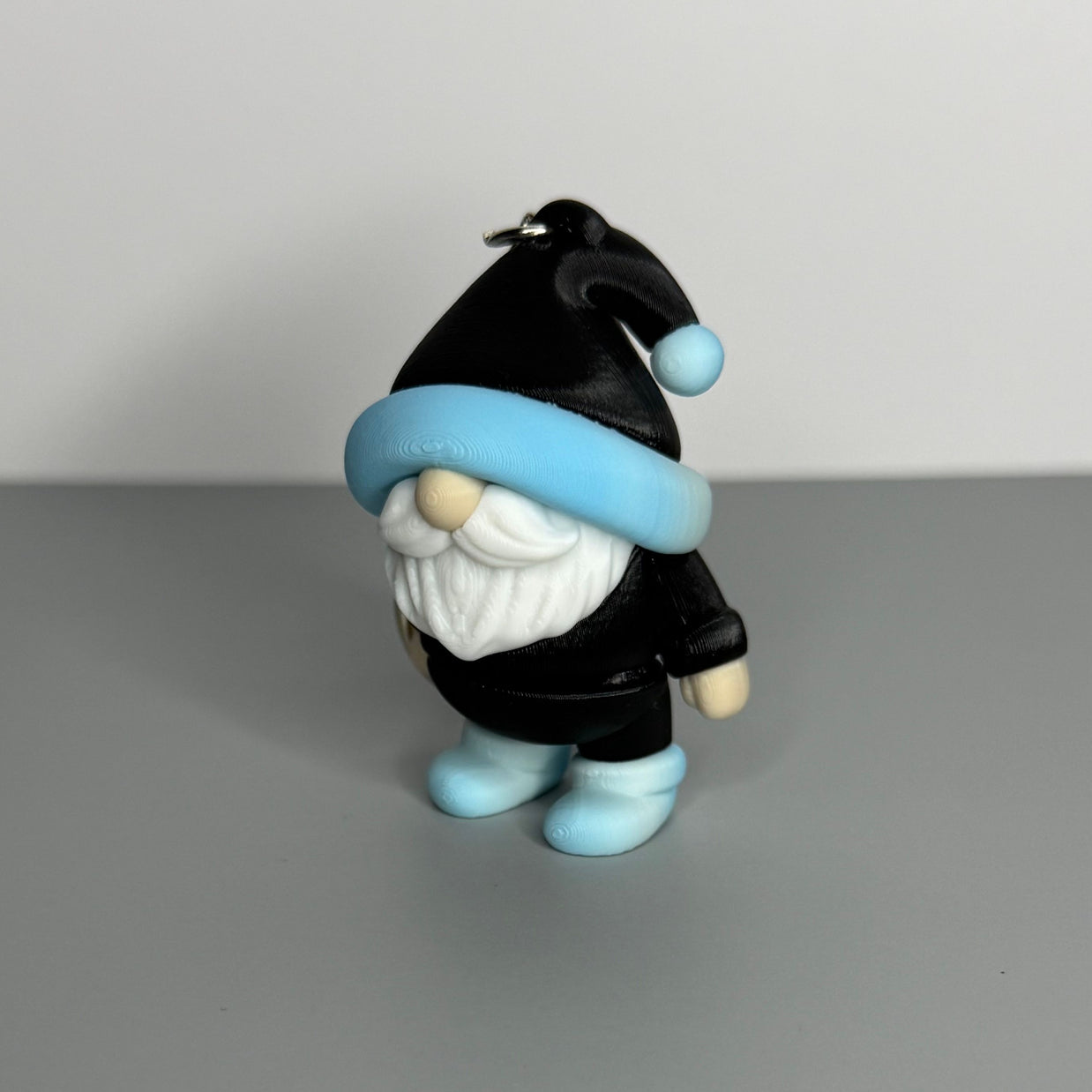 Gnome-shaped keychain in black with a blue/white gradient and black hat, white beard, and blue/white gradient shoes. 