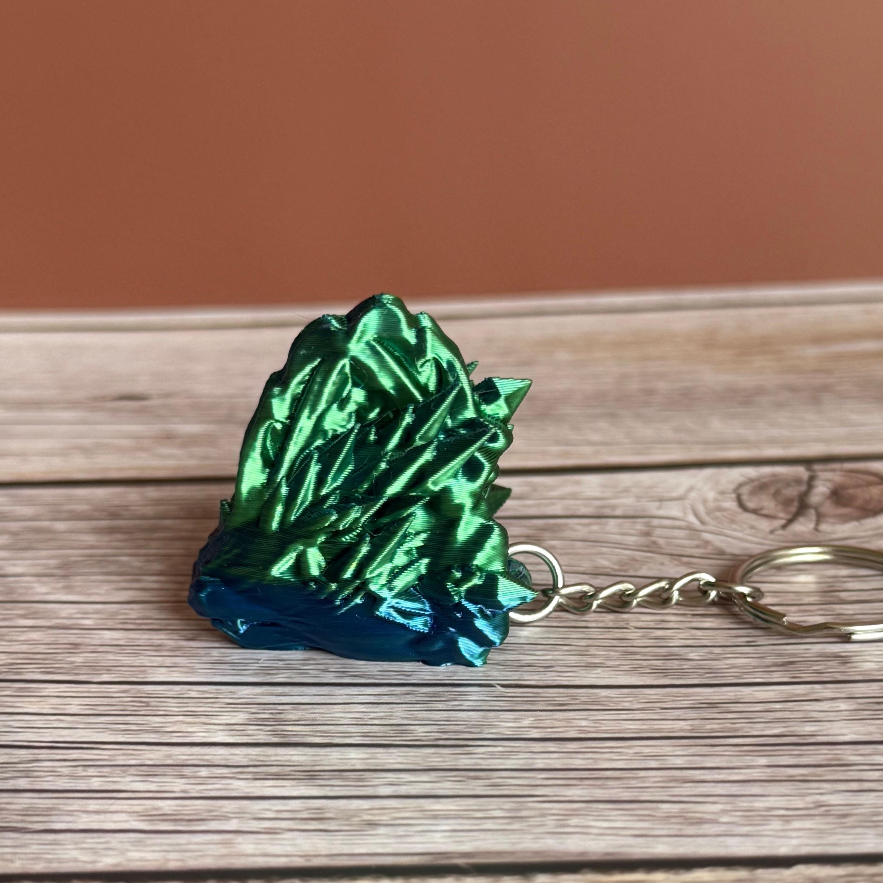 Side of a 3D printed blue and green jellyfish-themed dragon head keychain, placed on a wooden surface