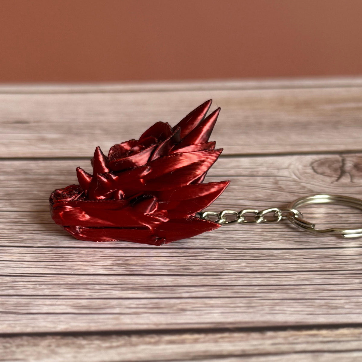 Primarily red side of a 3D printed red and black dragon head keychain with a rose design on a wooden surface