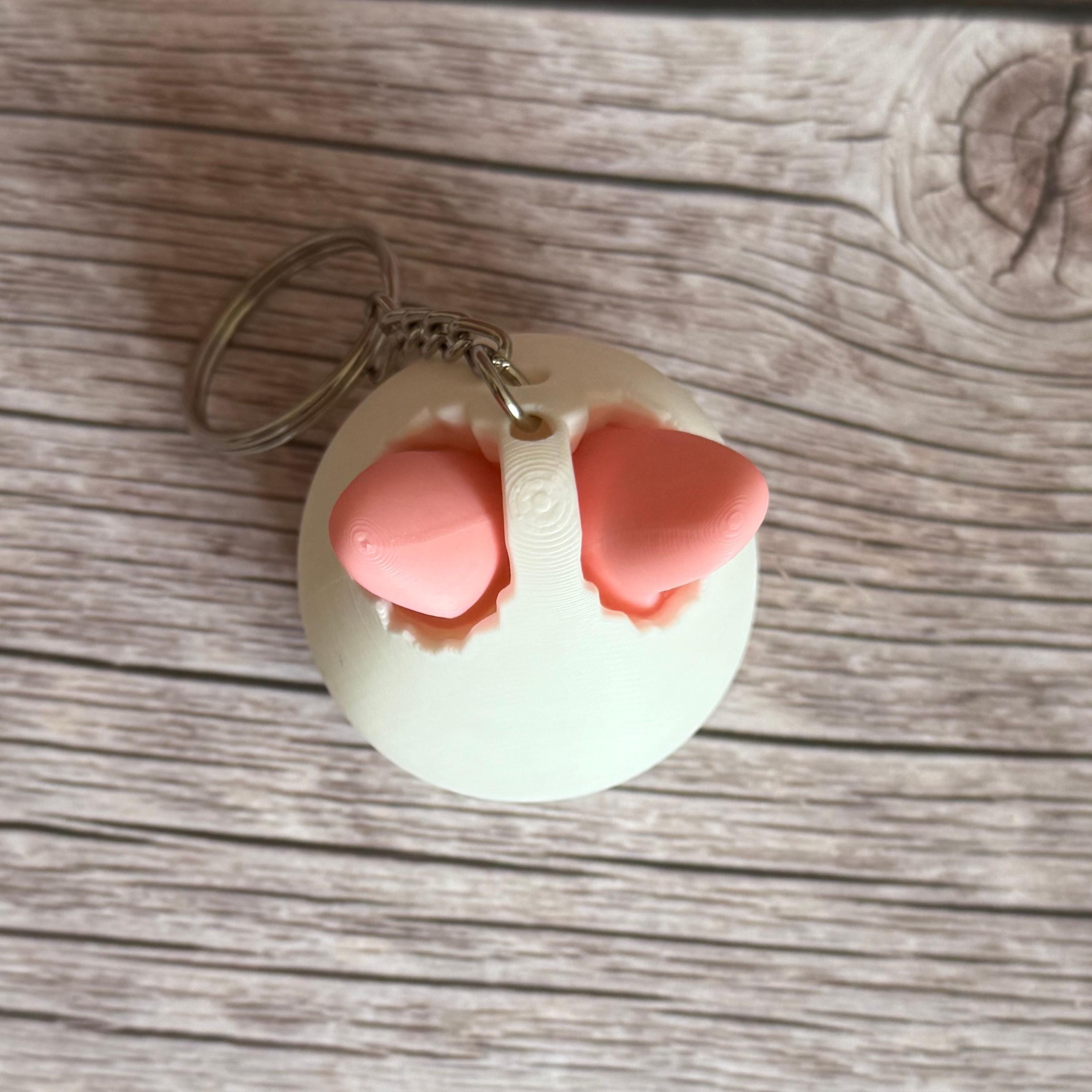 Top of a 3D printed white egg with pink bunny ears keychain on a wooden surface