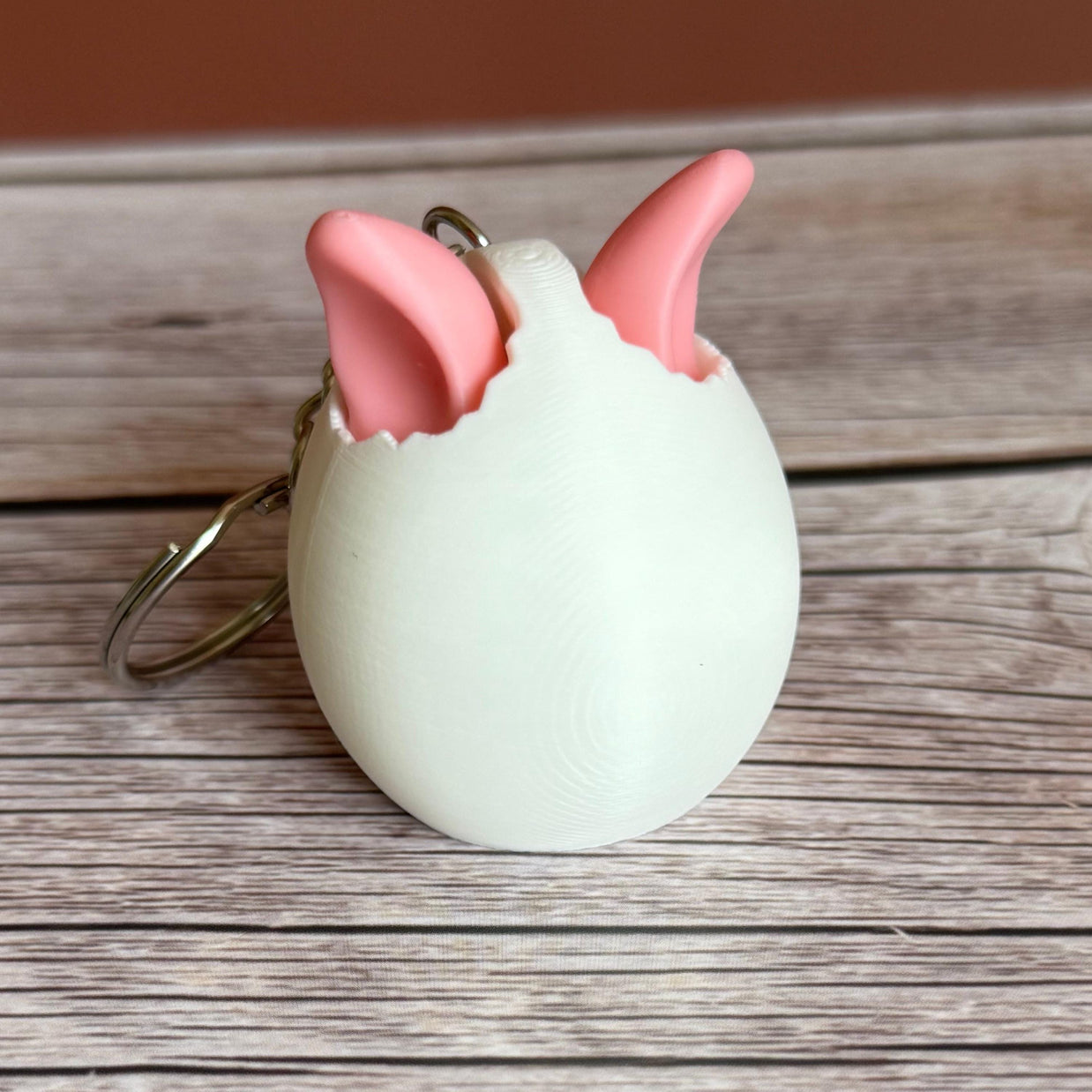 3D printed white egg with pink bunny ears keychain on a wooden surface