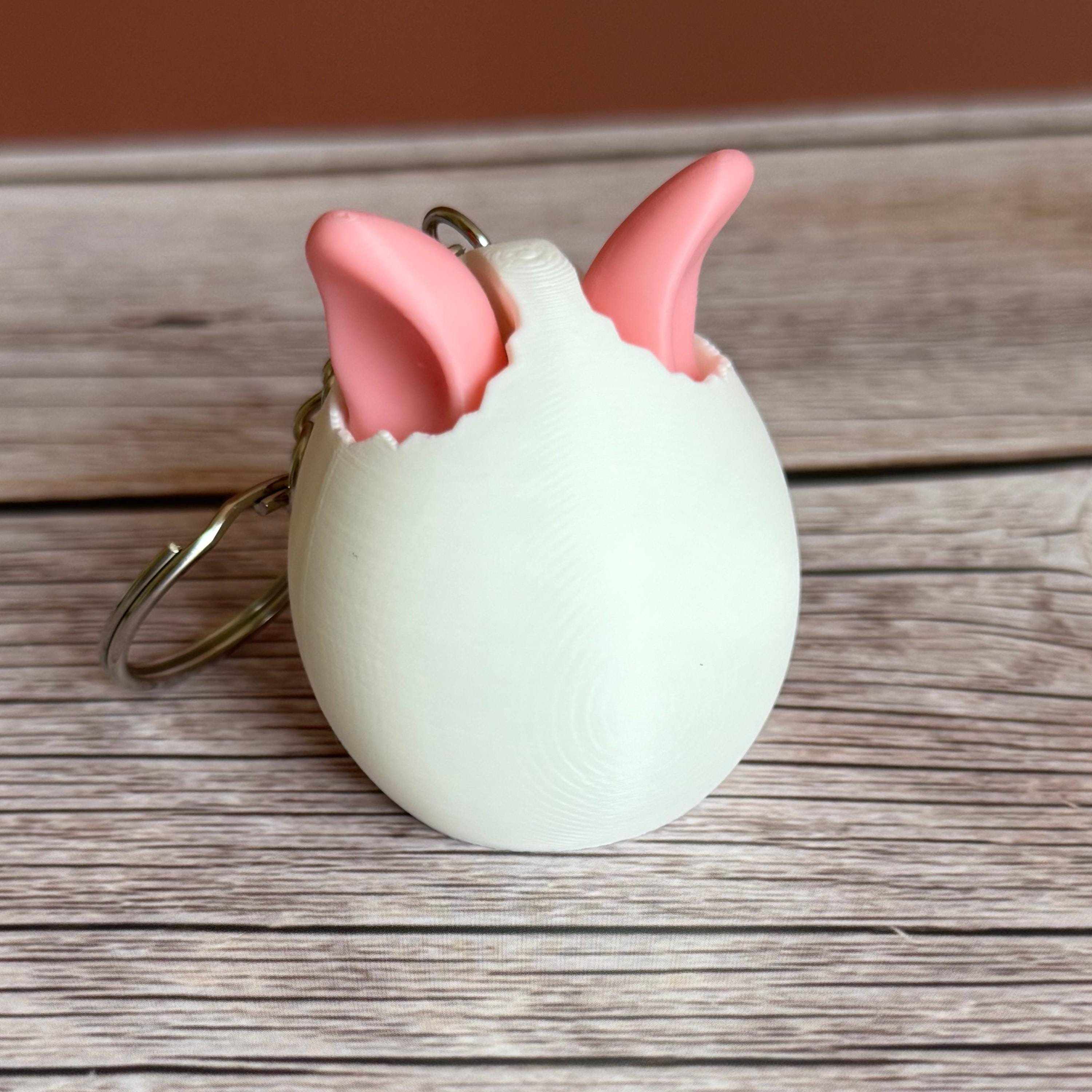 3D printed white egg with pink bunny ears keychain on a wooden surface