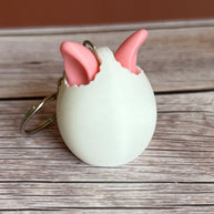 3D printed white egg with pink bunny ears keychain on a wooden surface