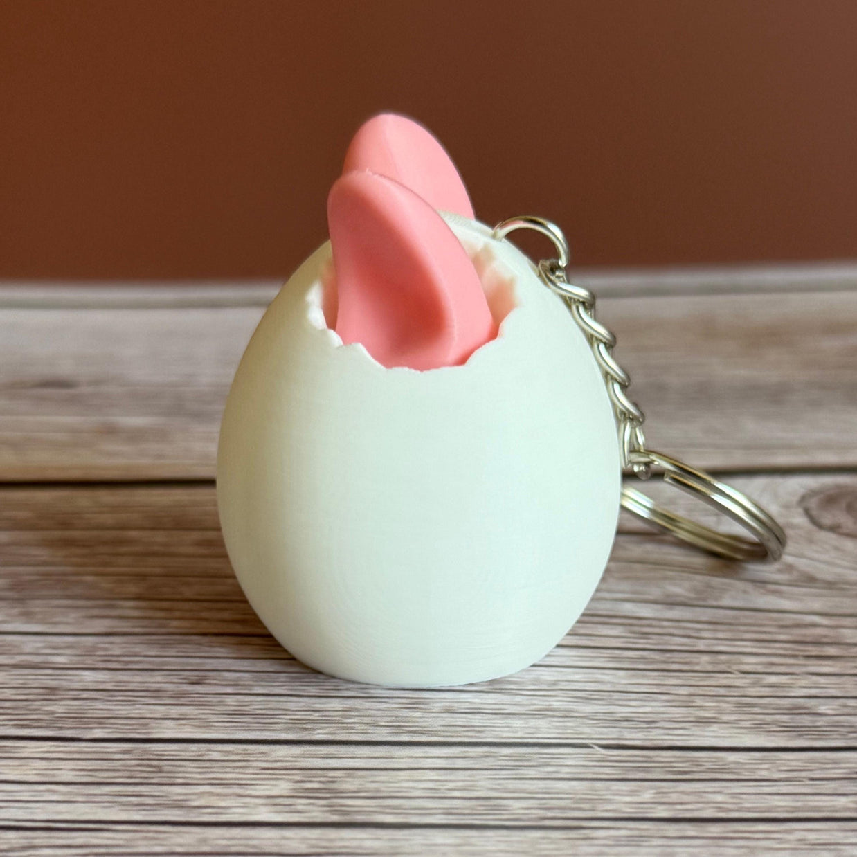 Side of a 3D printed white egg with pink bunny ears keychain on a wooden surface