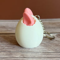 Side of a 3D printed white egg with pink bunny ears keychain on a wooden surface