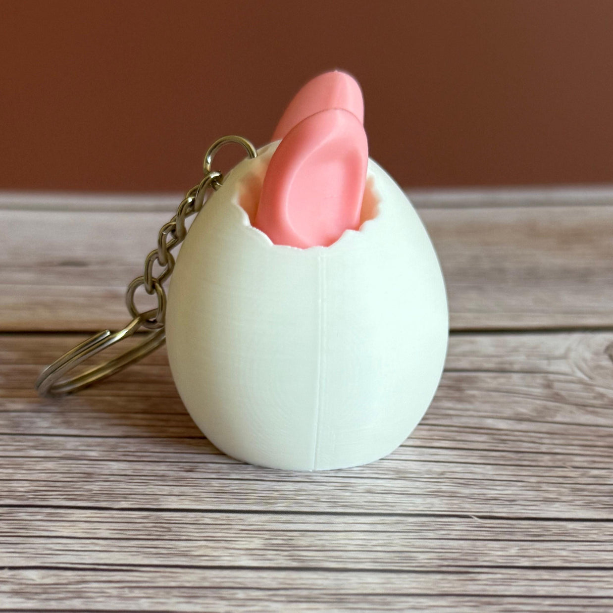 side of a 3D printed white egg with pink bunny ears keychain on a wooden surface