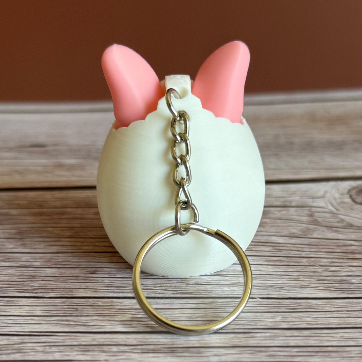 Back of a 3D printed white egg with pink bunny ears keychain on a wooden surface