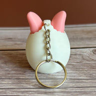 Back of a 3D printed white egg with pink bunny ears keychain on a wooden surface