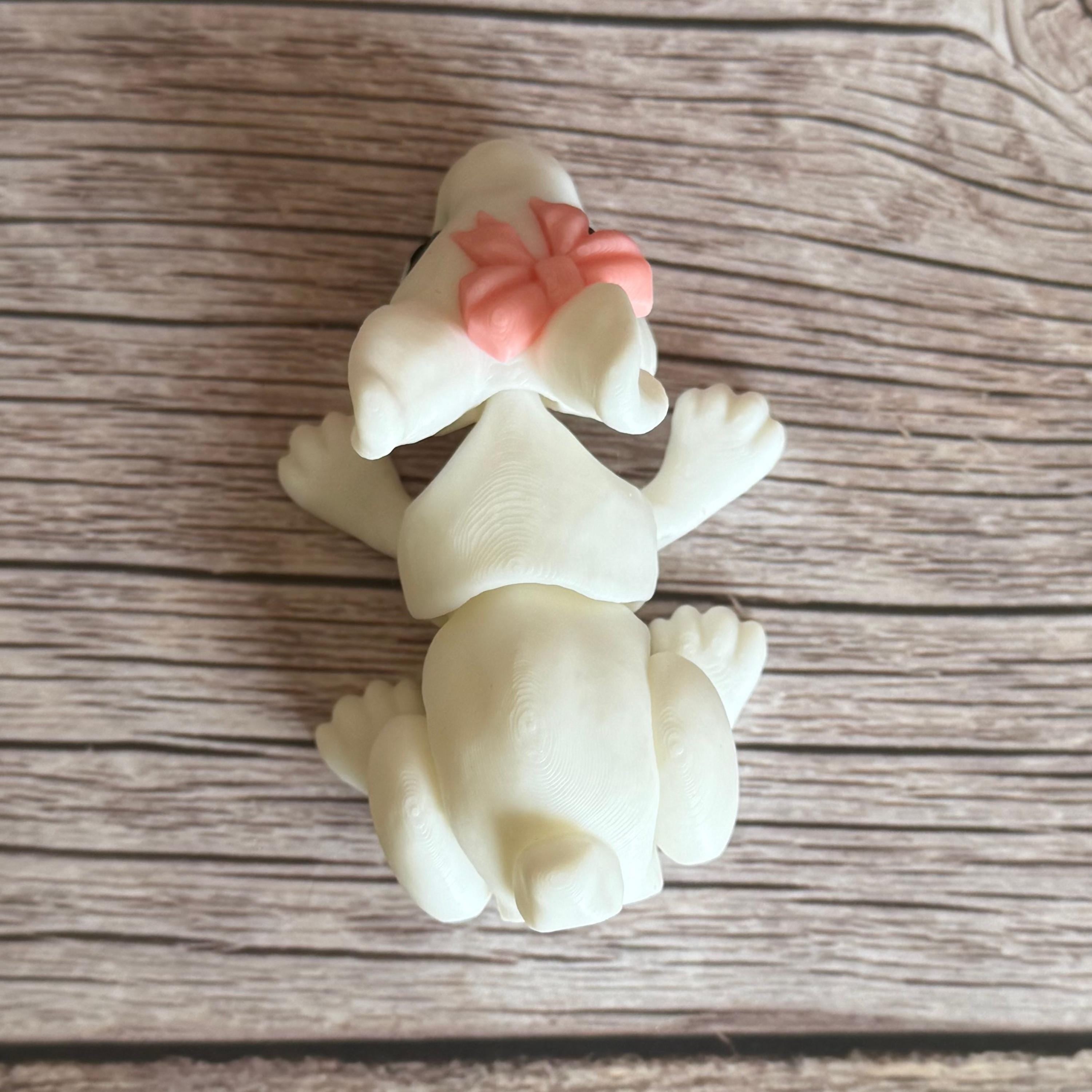 Top of a 3D printed white rabbit figurine with a pink bow on a wooden surface