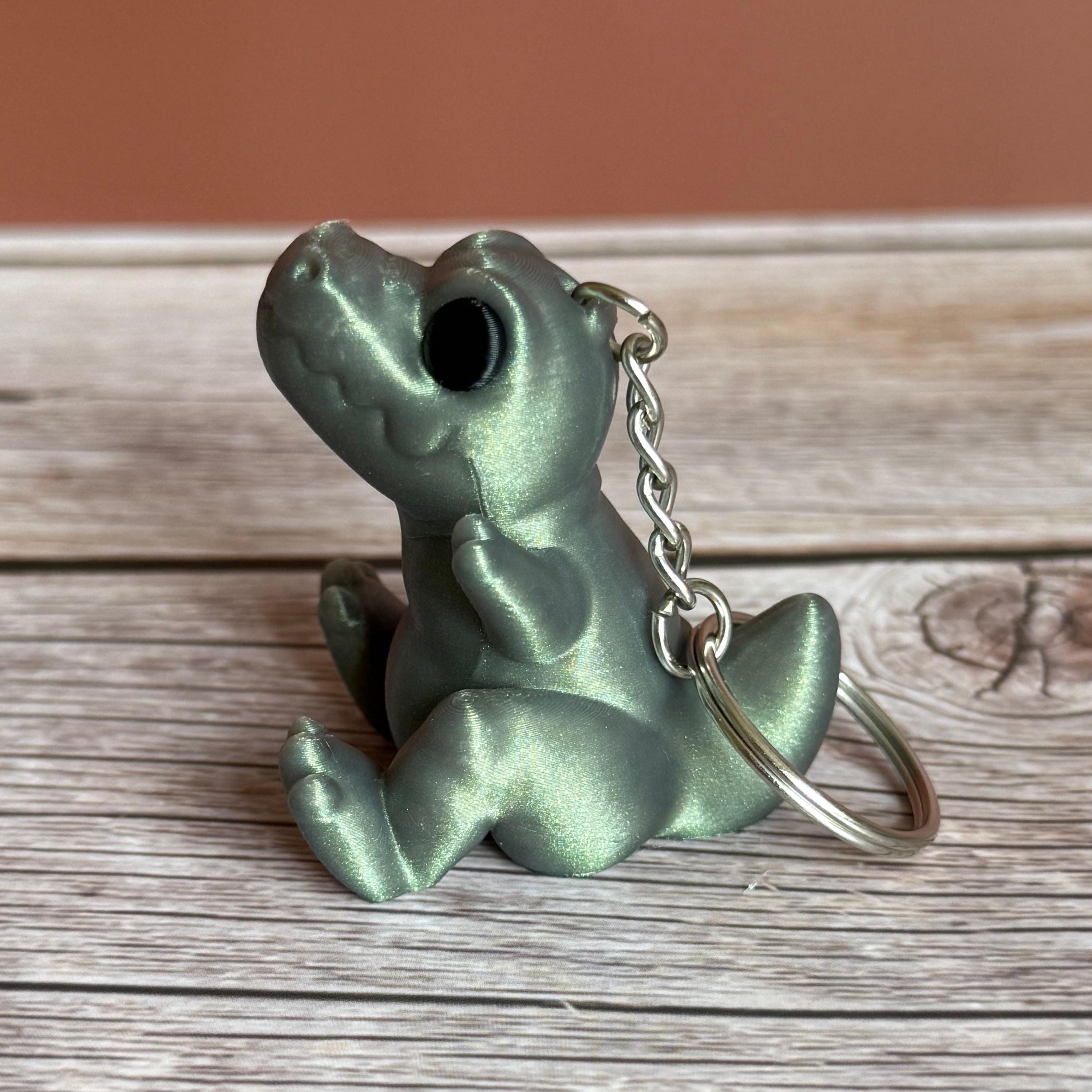 Side of a 3D printed shimmer-green T-Rex dinosaur keychain on a wooden surface