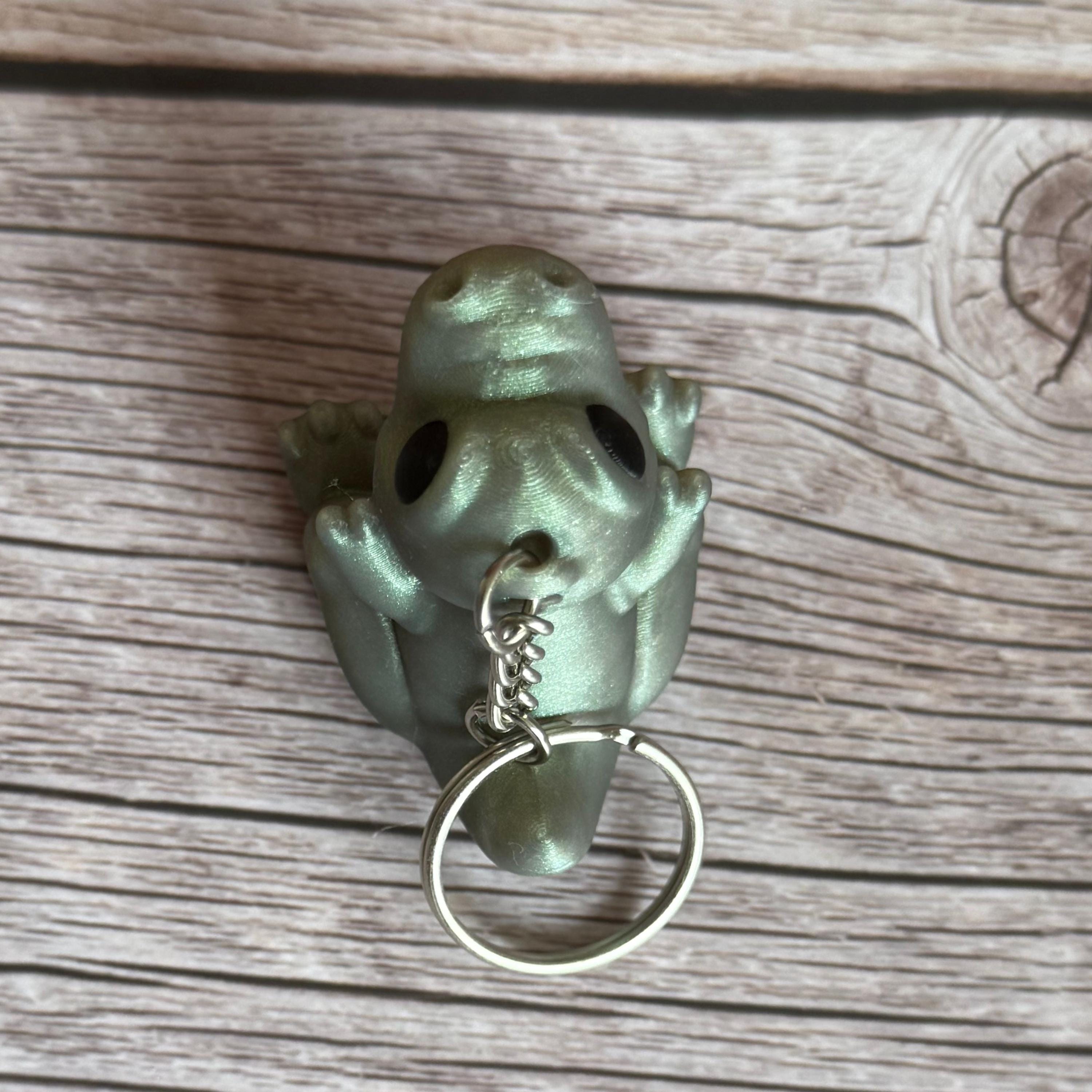 Top of a 3D printed shimmer-green T-Rex dinosaur keychain on a wooden surface