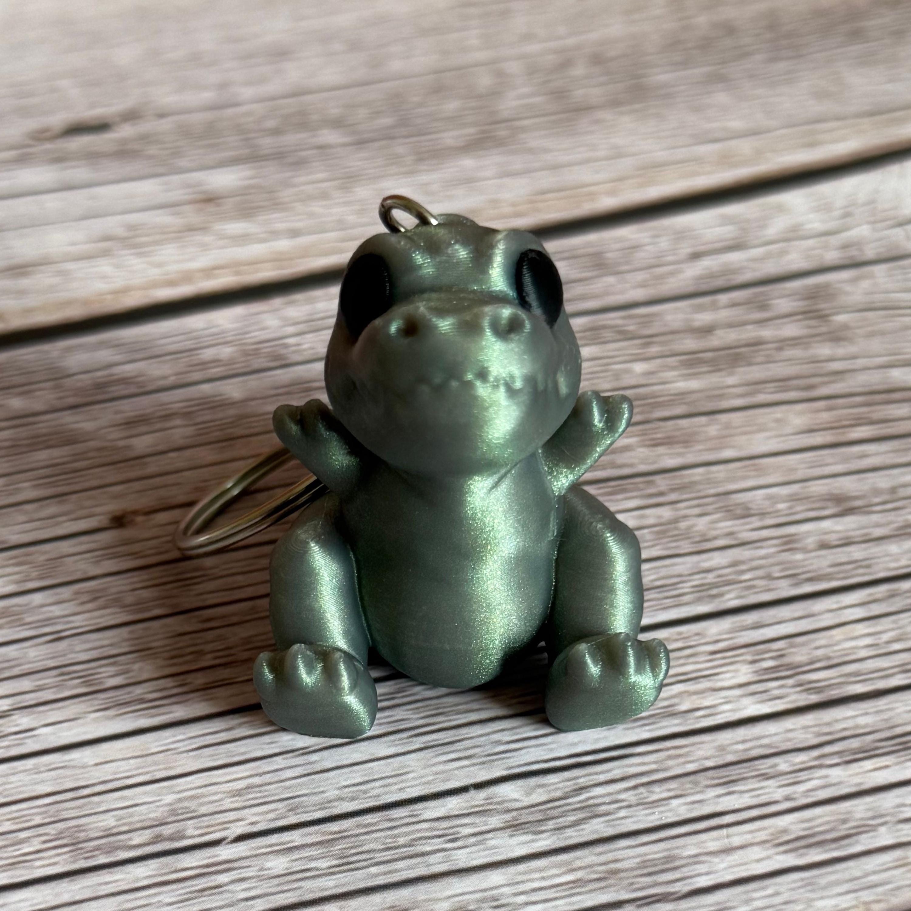 Front of a 3D printed shimmer-green T-Rex dinosaur keychain on a wooden surface