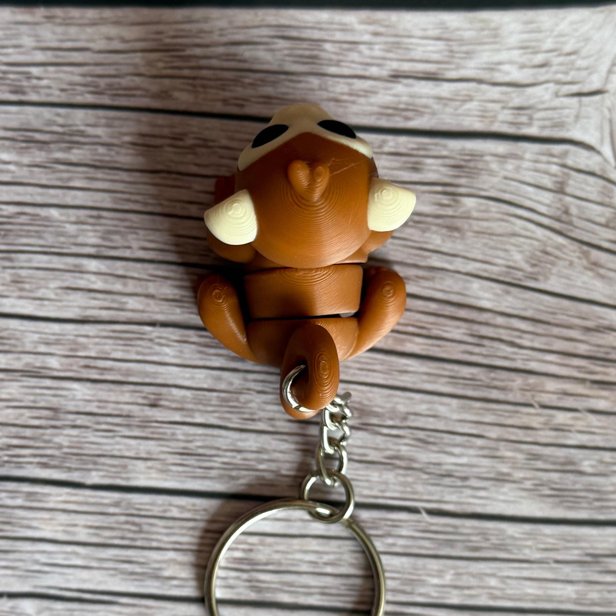Top of a 3D printed brown monkey-shaped keychain on a wooden surface