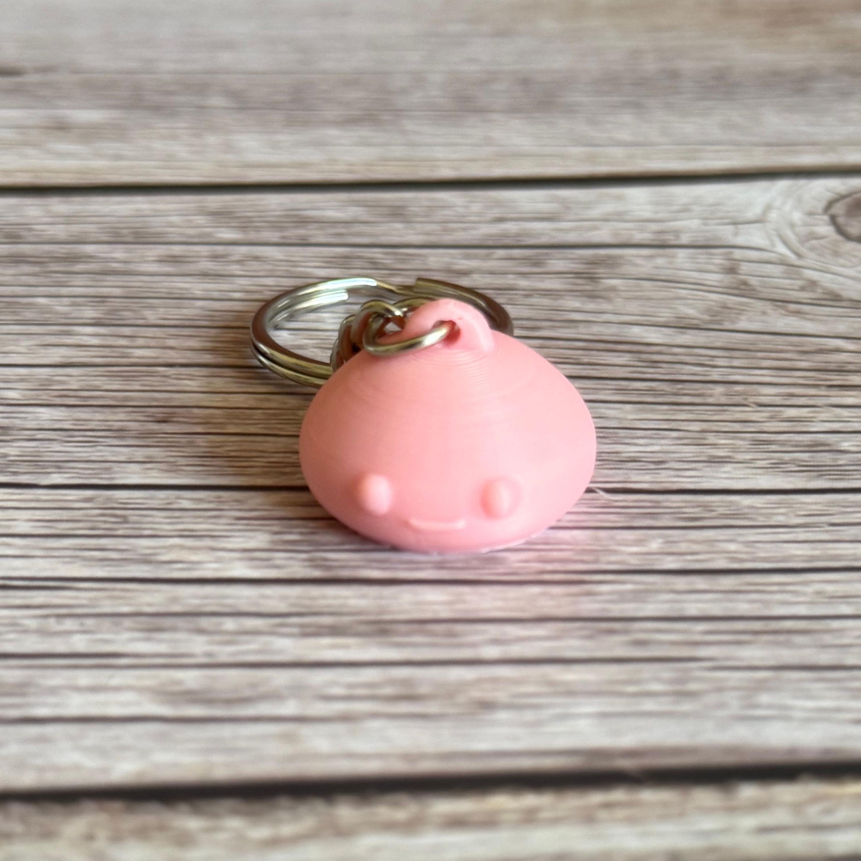 3D Printed pink jellyfish-like keychain with body hidden inside head on a wooden surface