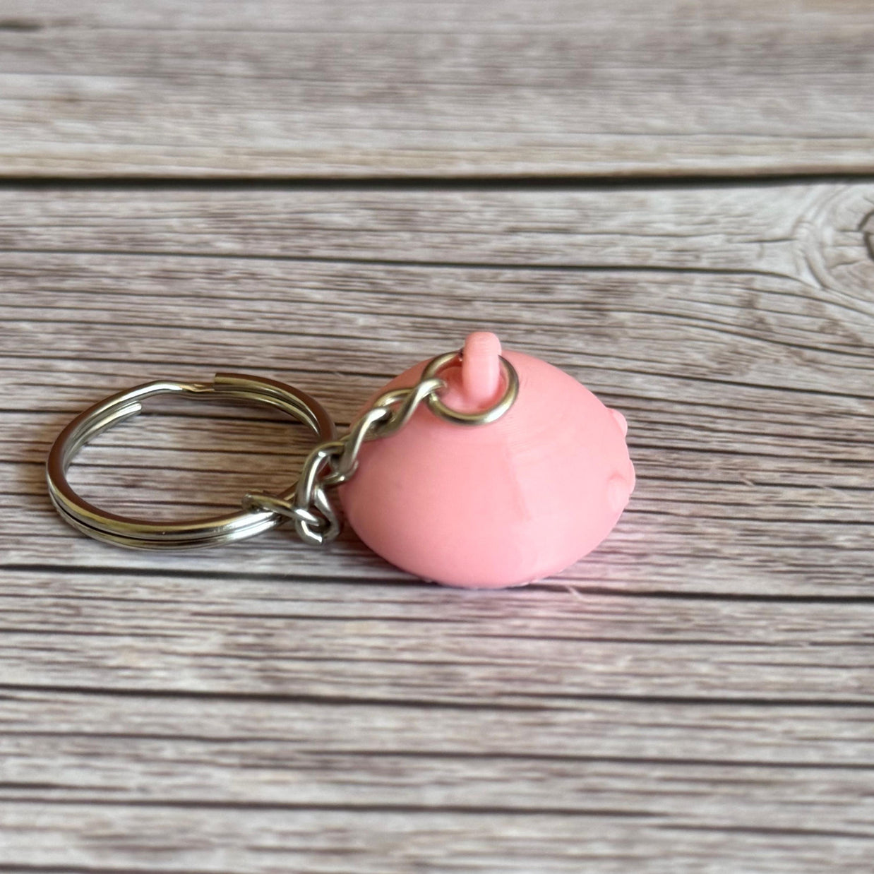 3D Printed pink jellyfish-like keychain with body hidden inside head on a wooden surface