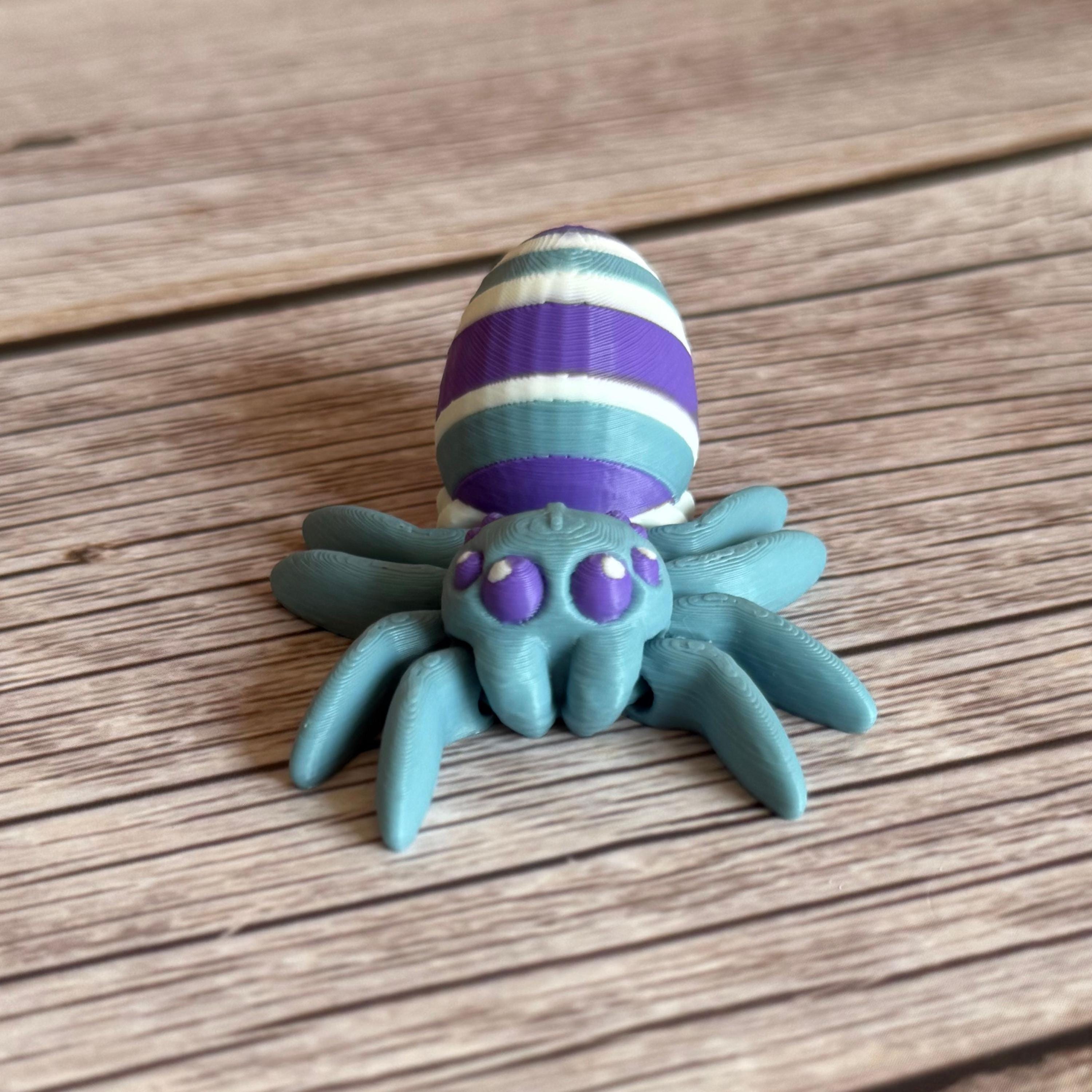 3D printed blue spider featuring a white, blue, and purple egg on its body, placed on a wooden surface