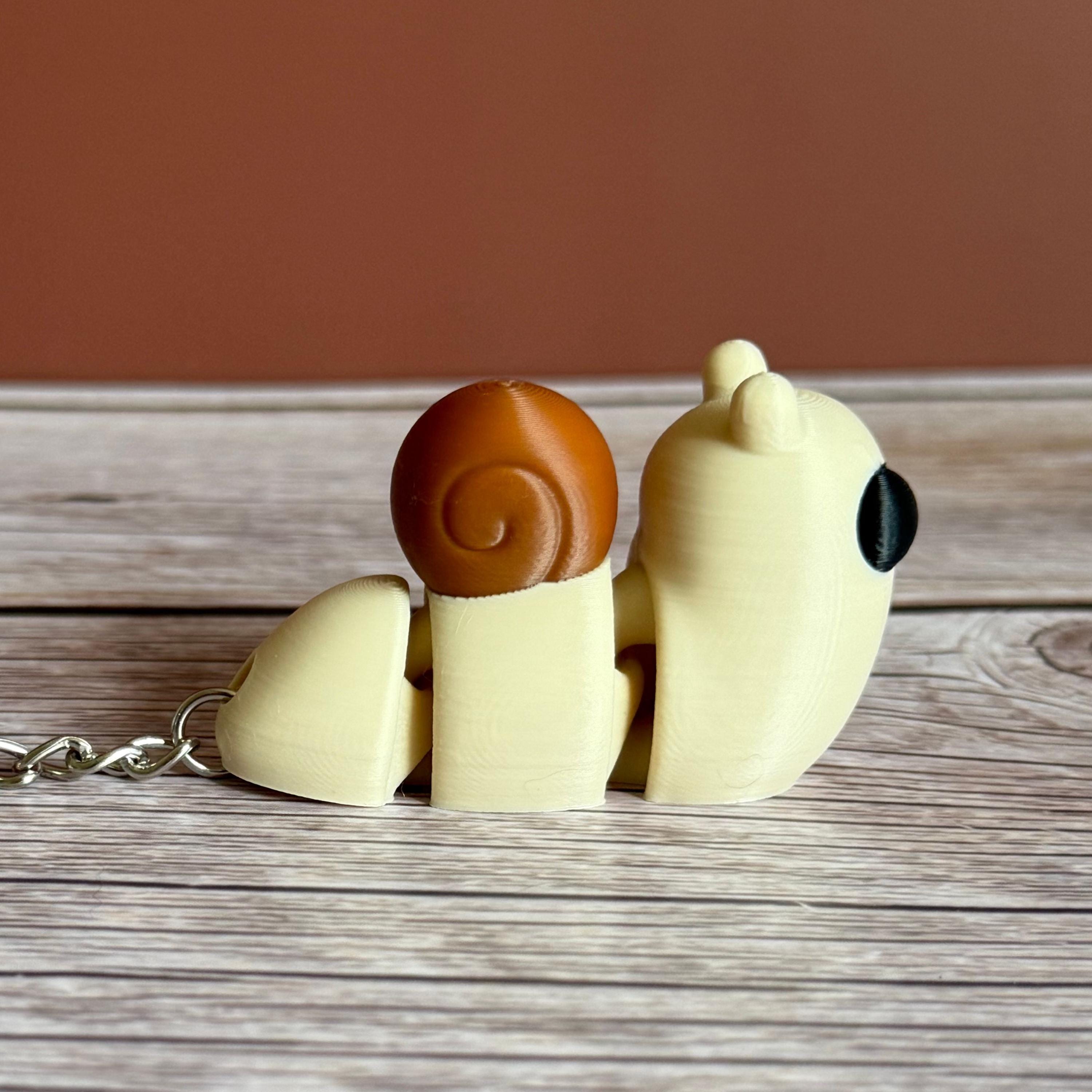 Side of a 3D printed beige and brown snail-shaped keychain on a wooden surface