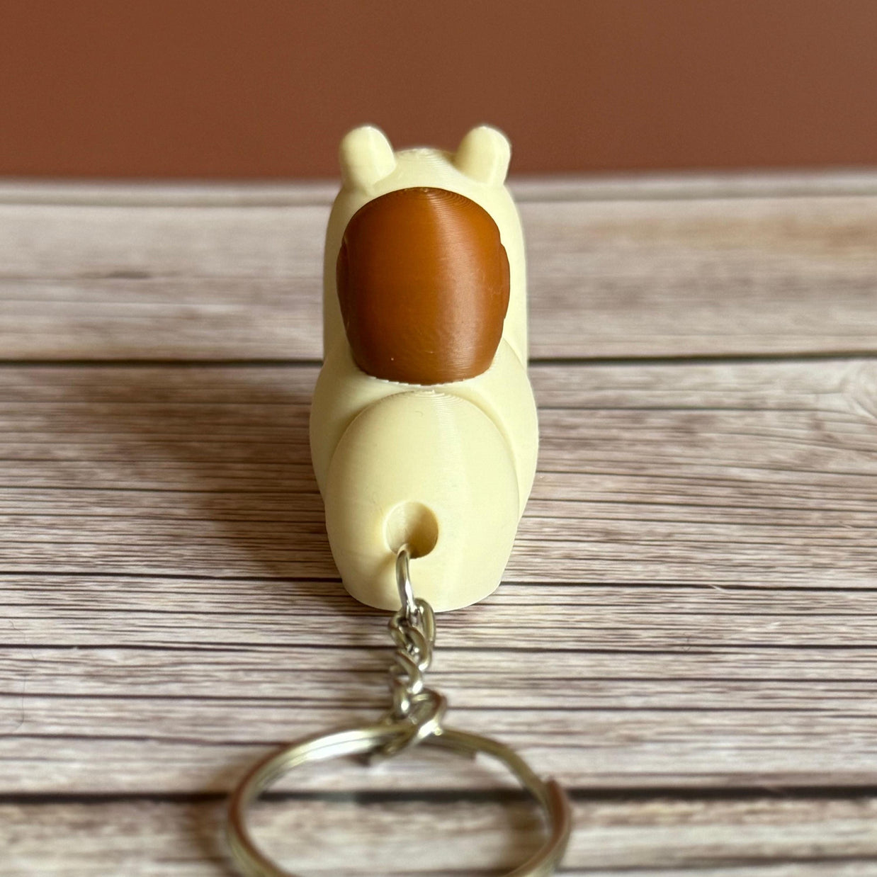 Back of a 3D printed beige and brown snail-shaped keychain on a wooden surface