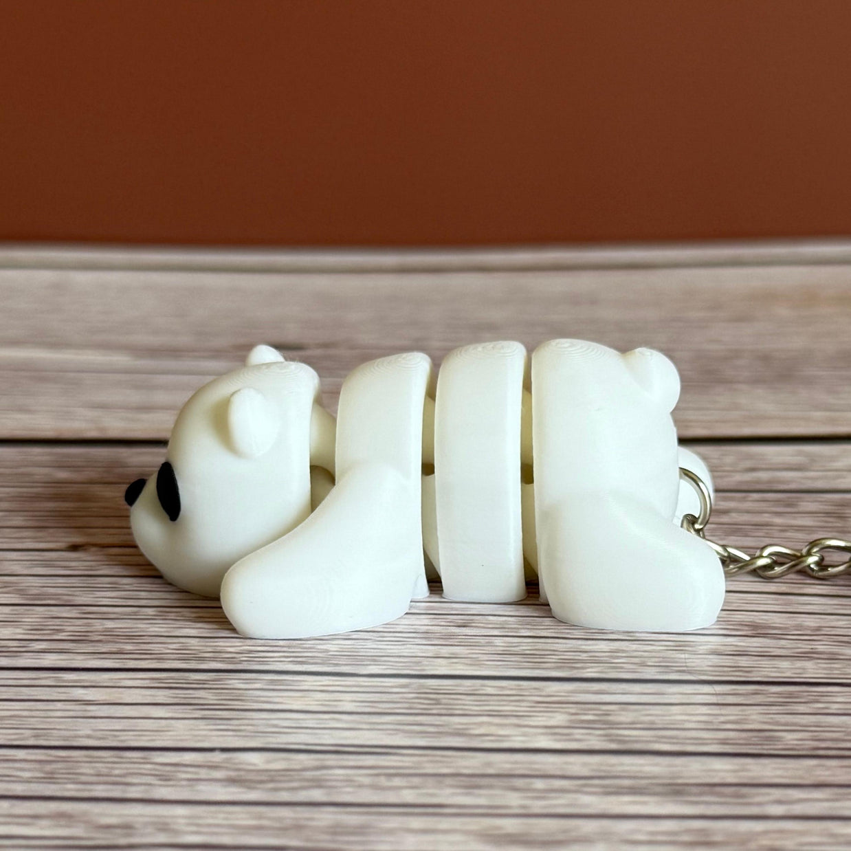 Side of a 3D printed white bear-shaped keychain on a wooden surface