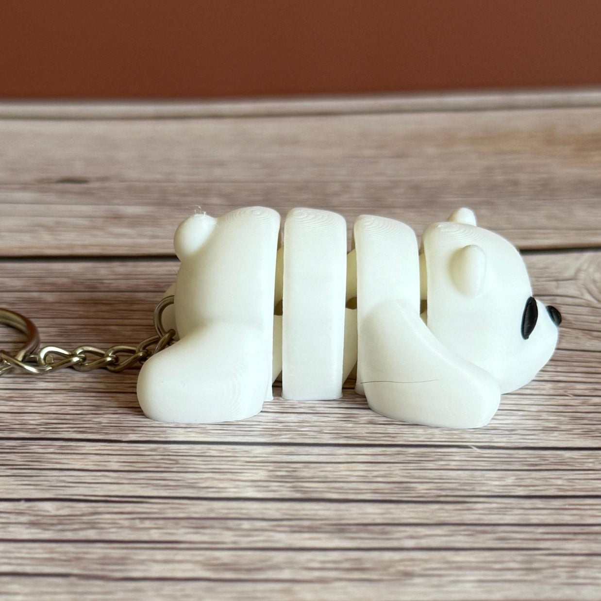 Side of a 3D printed white bear-shaped keychain on a wooden surface