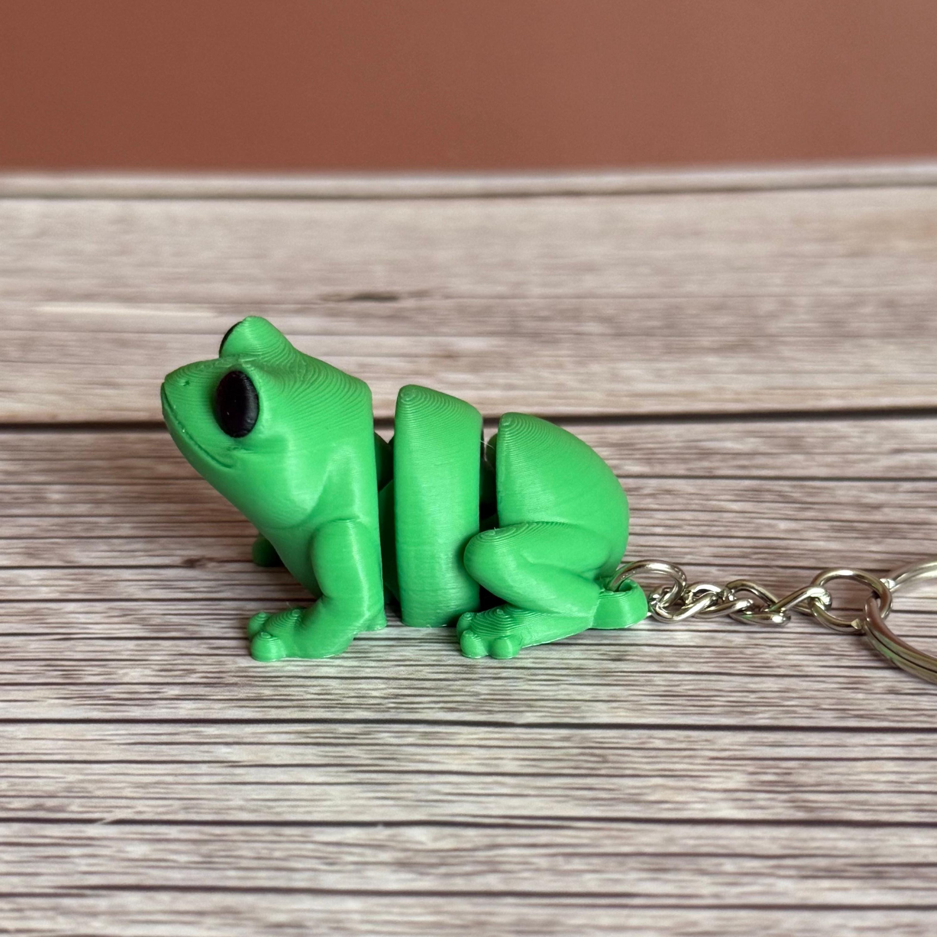 Side of a 3D printed green frog-shaped keychain on a wooden surface