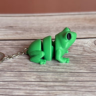 Side of a 3D printed green frog-shaped keychain on a wooden surface