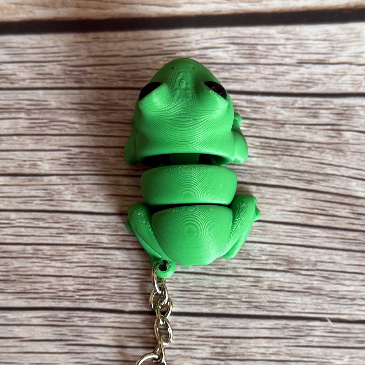 Top of a 3D printed green frog-shaped keychain on a wooden surface