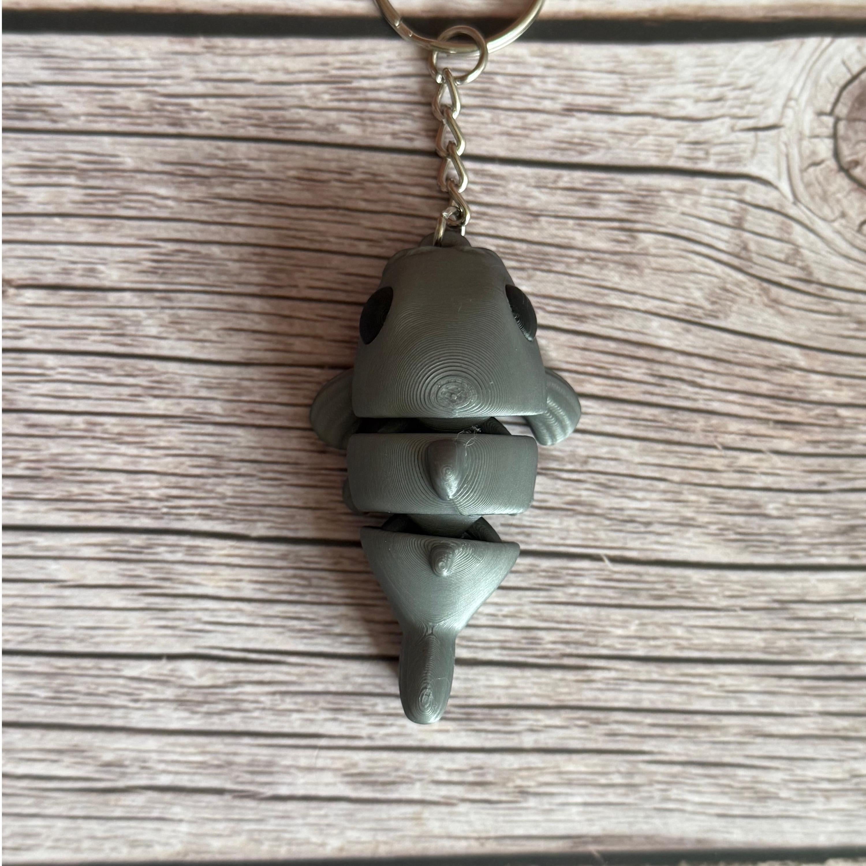 Top of a 3D printed gray catfish-shaped keychain on a wooden surface
