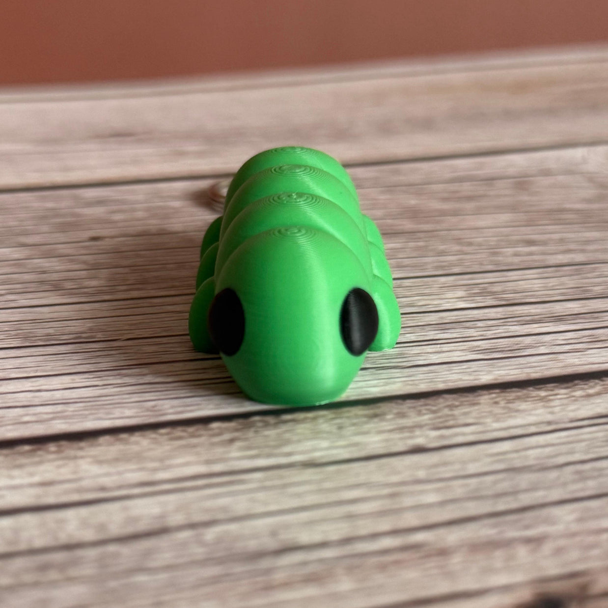 3D printed green caterpillar-shaped keychain on a wooden surface