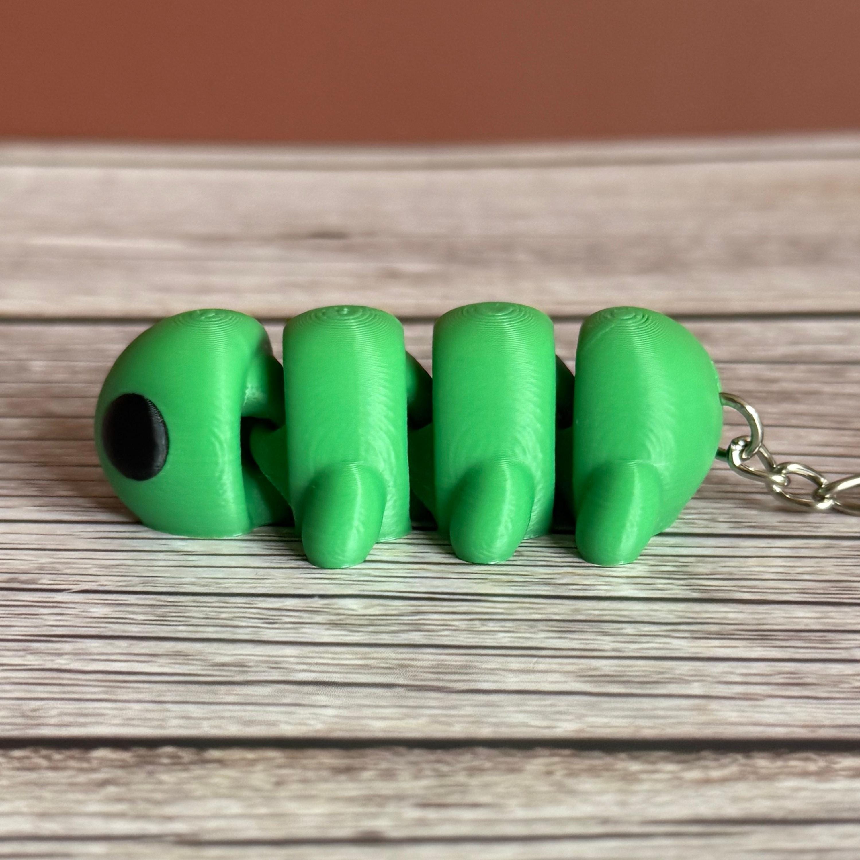 Side of a 3D printed green caterpillar-shaped keychain on a wooden surface