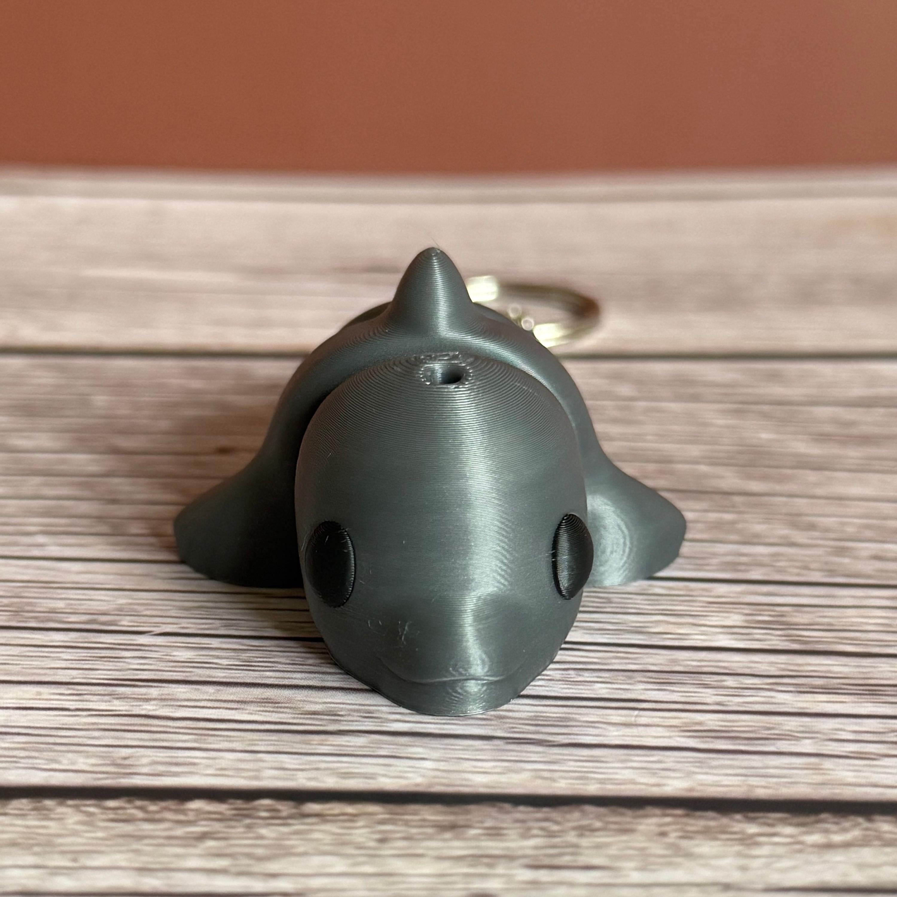 3D printed gray dolphin-shaped keychain on a wooden surface
