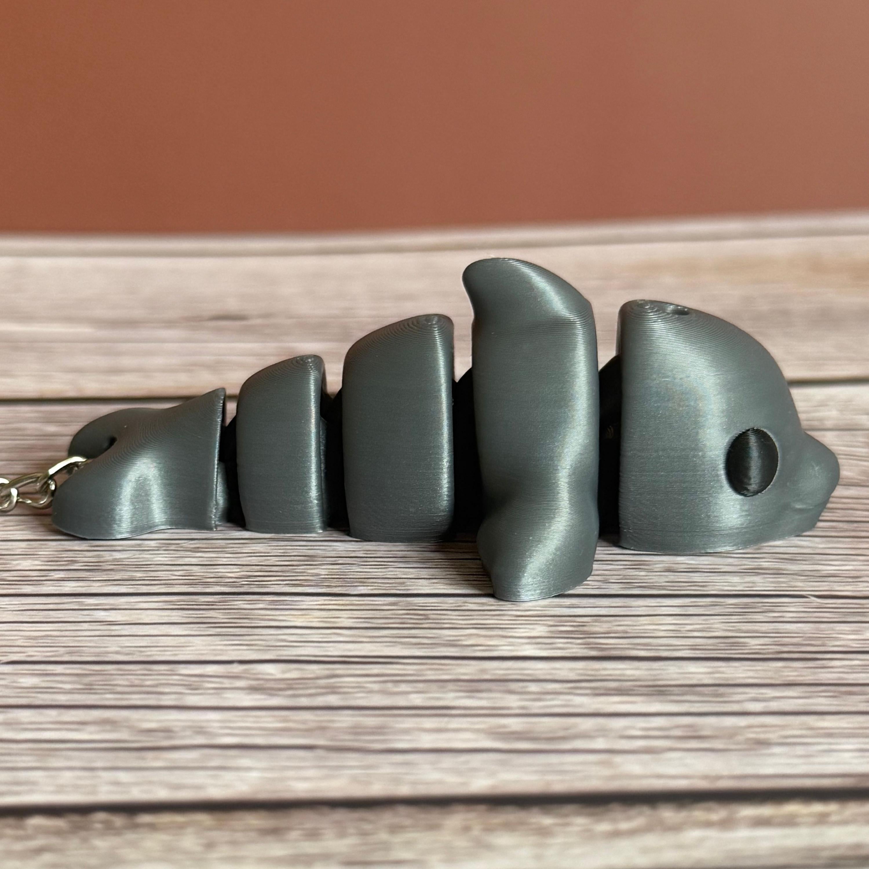Side of a 3D printed gray dolphin-shaped keychain on a wooden surface