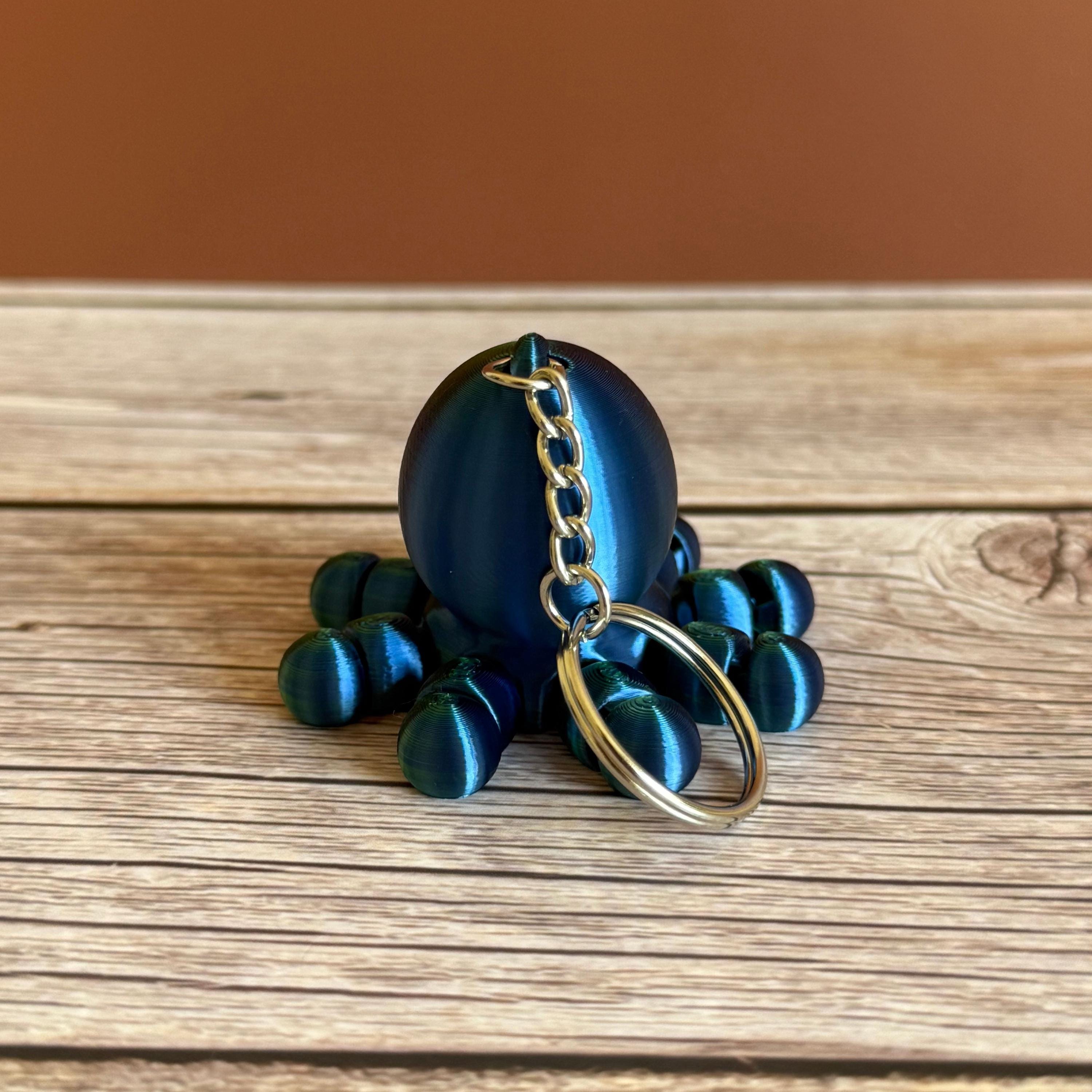 3D printed shiny green and blue octopus-shaped keychain, placed on a wooden surface with a brown background