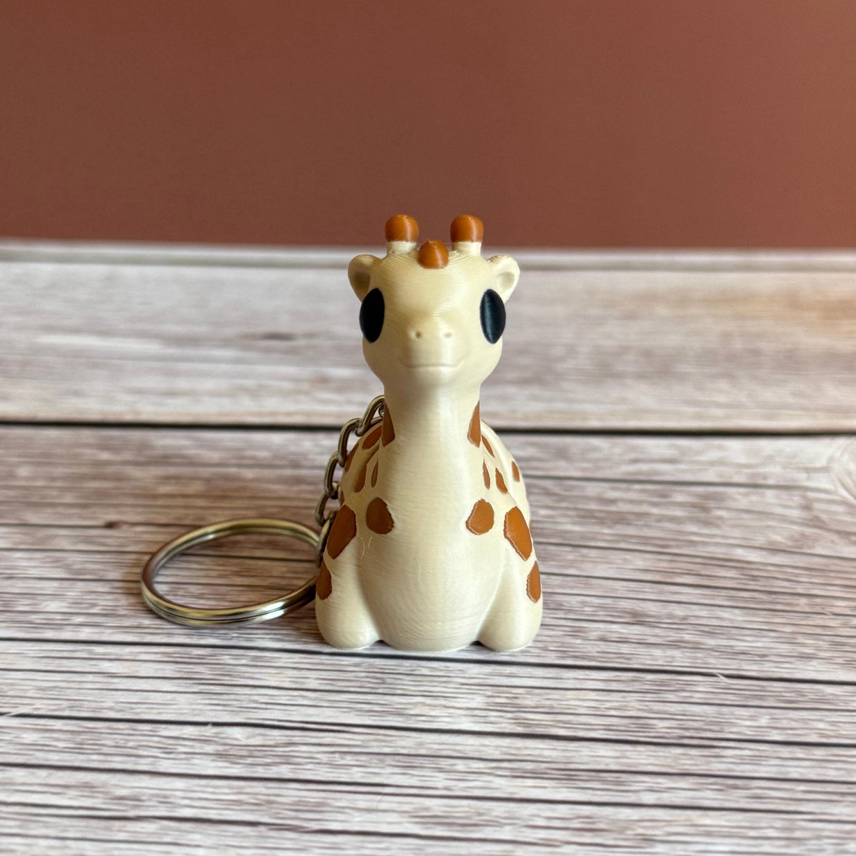 3D printed beige and brown giraffe-shaped keychain, placed on a wooden surface against a brown background