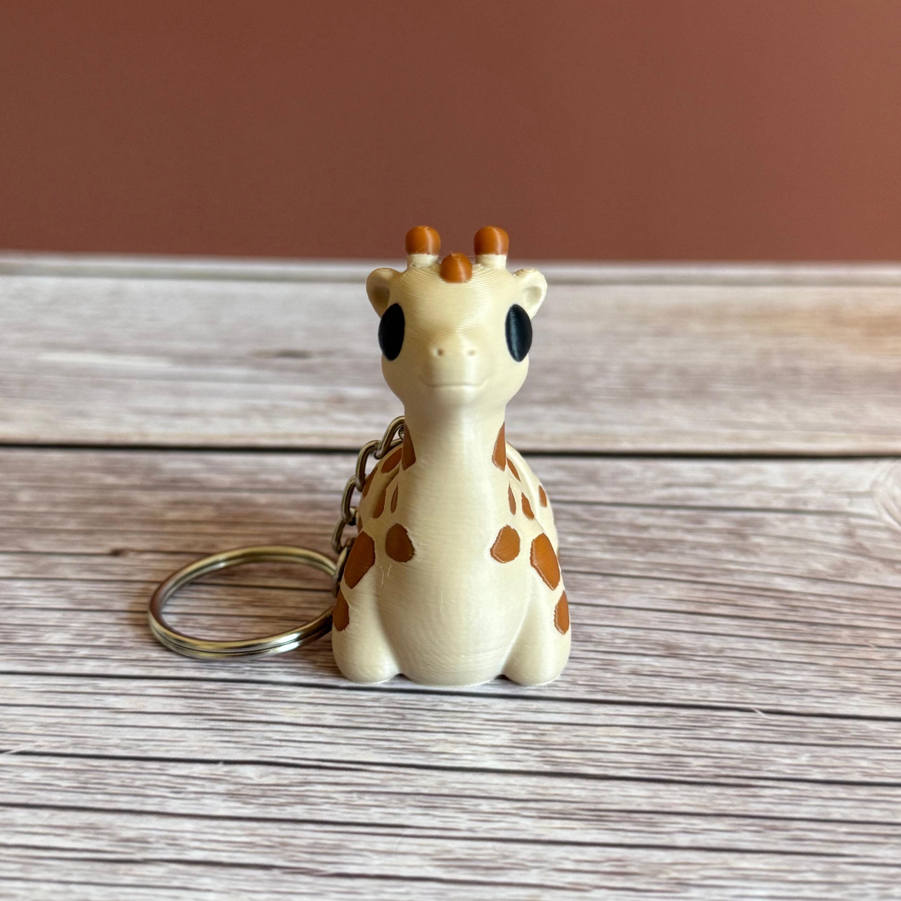 3D printed beige and brown giraffe-shaped keychain, placed on a wooden surface against a brown background