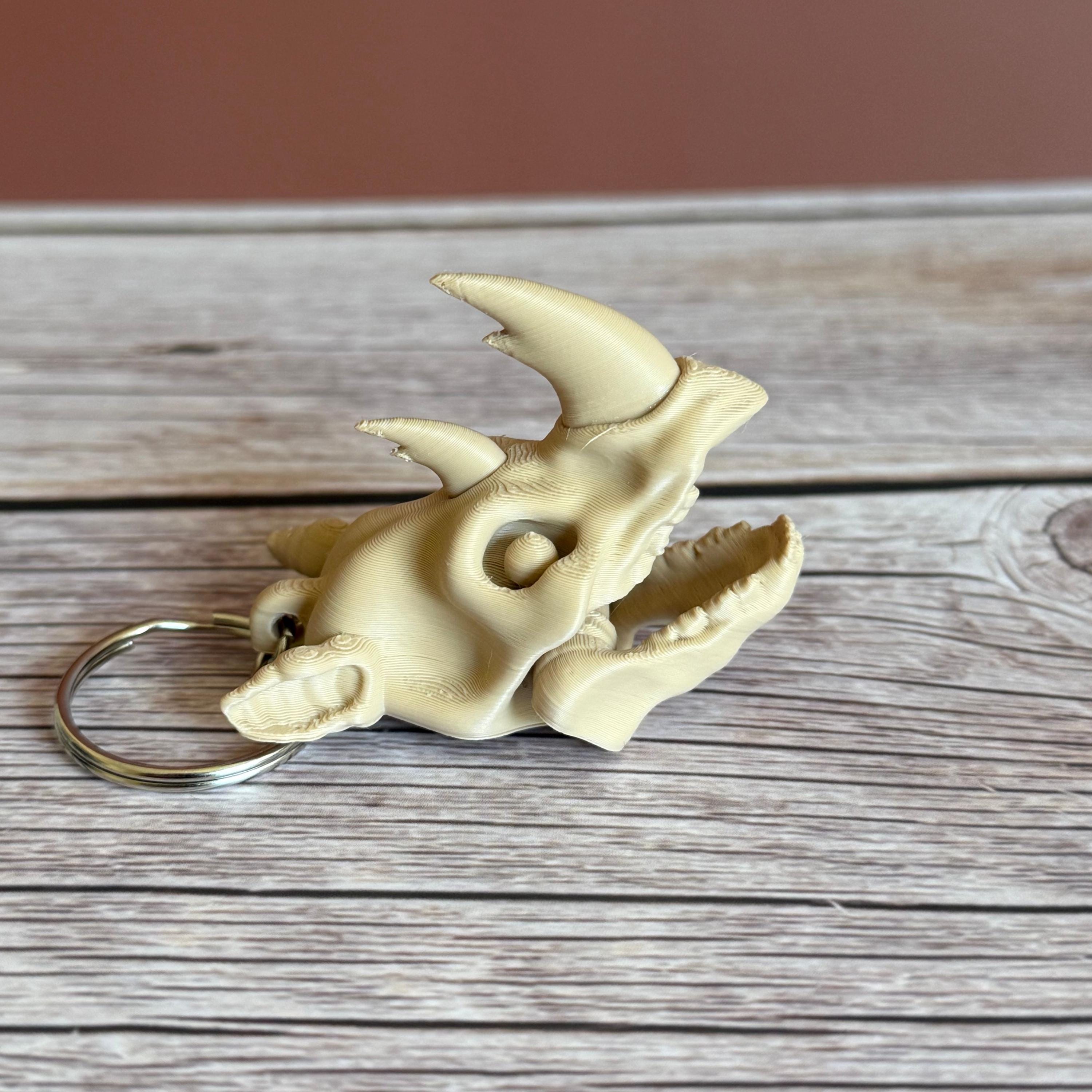 3D printed beige rhino skull keychain, placed on a wooden surface with a brown background