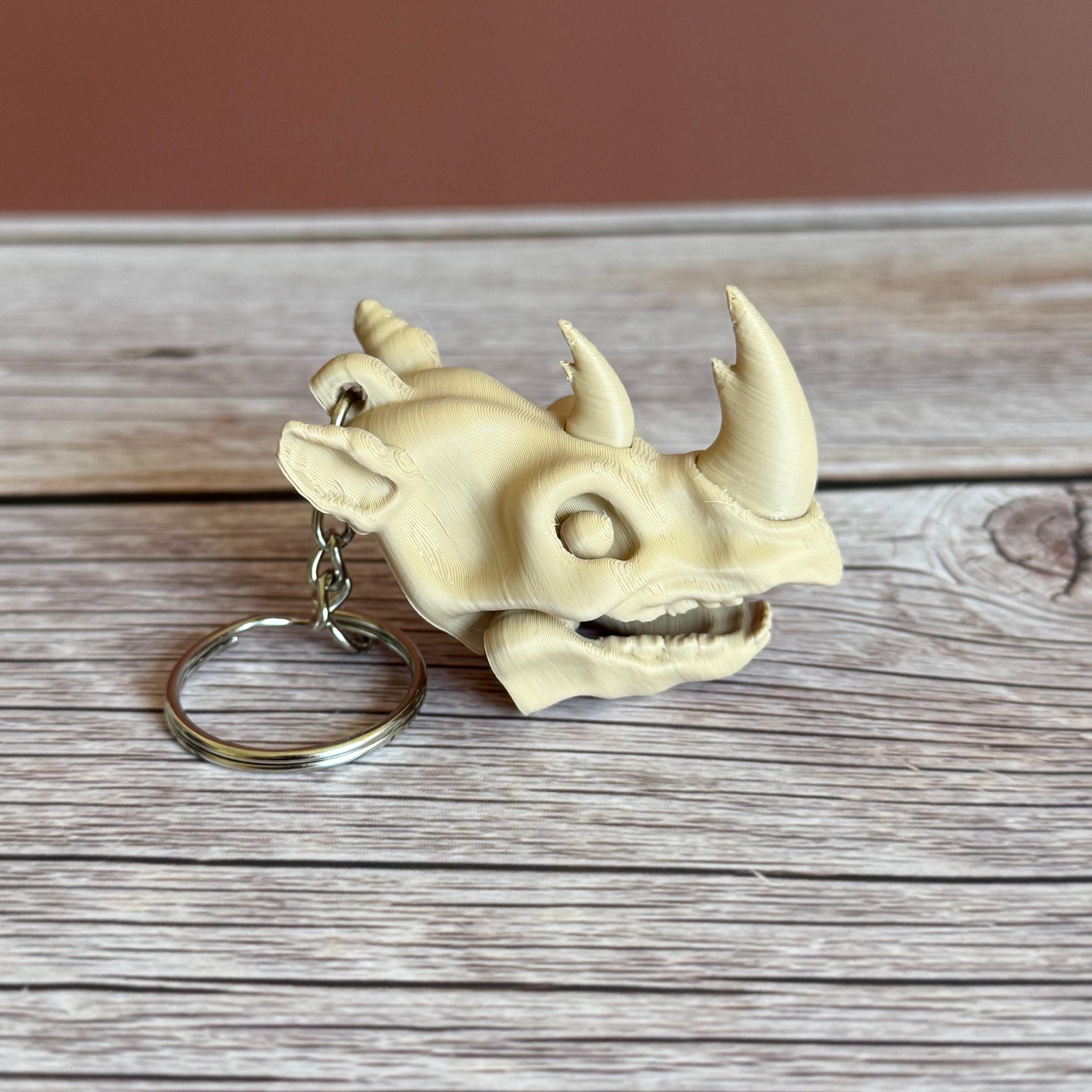 3D printed beige rhino skull keychain, placed on a wooden surface with a brown background