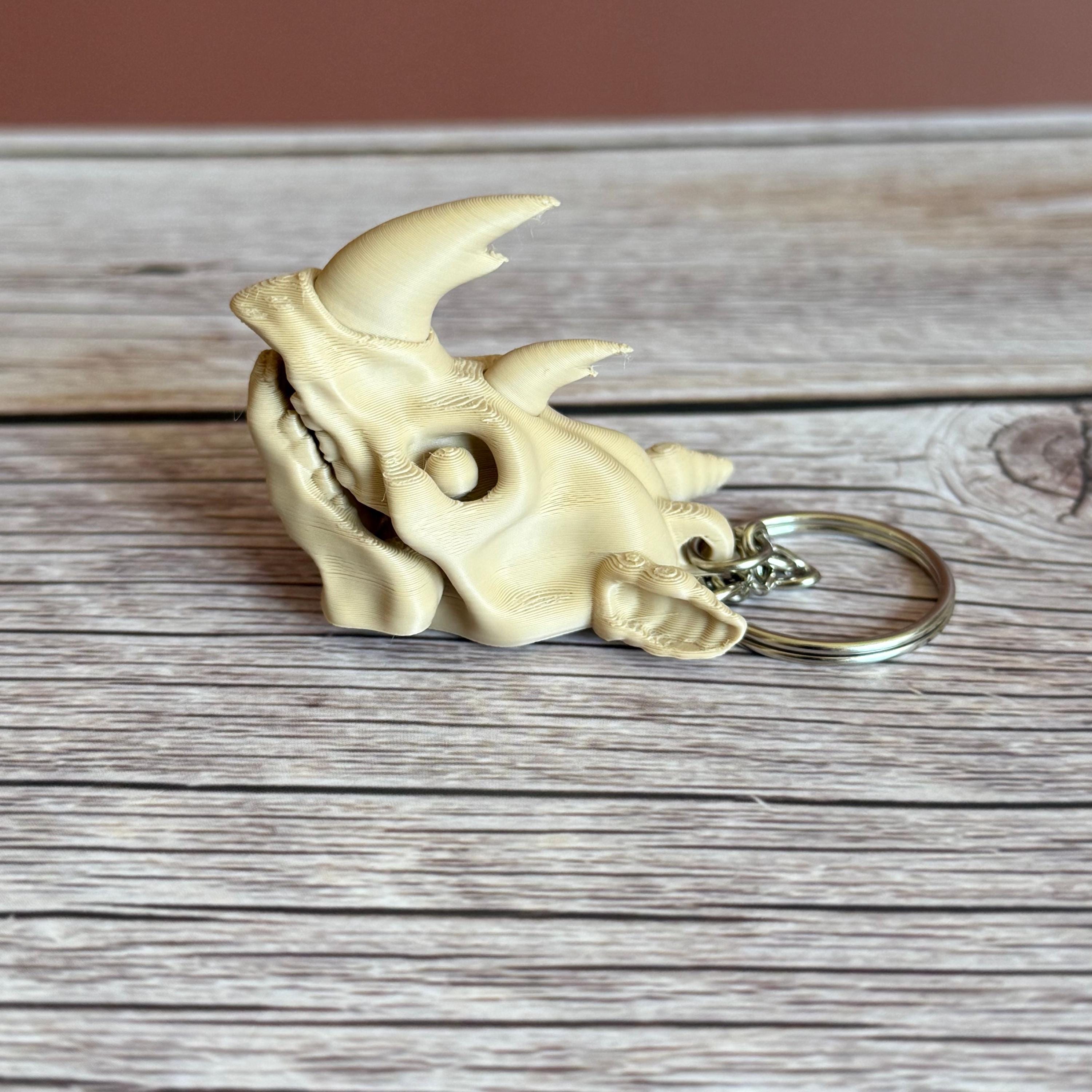 3D printed beige rhino skull keychain, placed on a wooden surface with a brown background