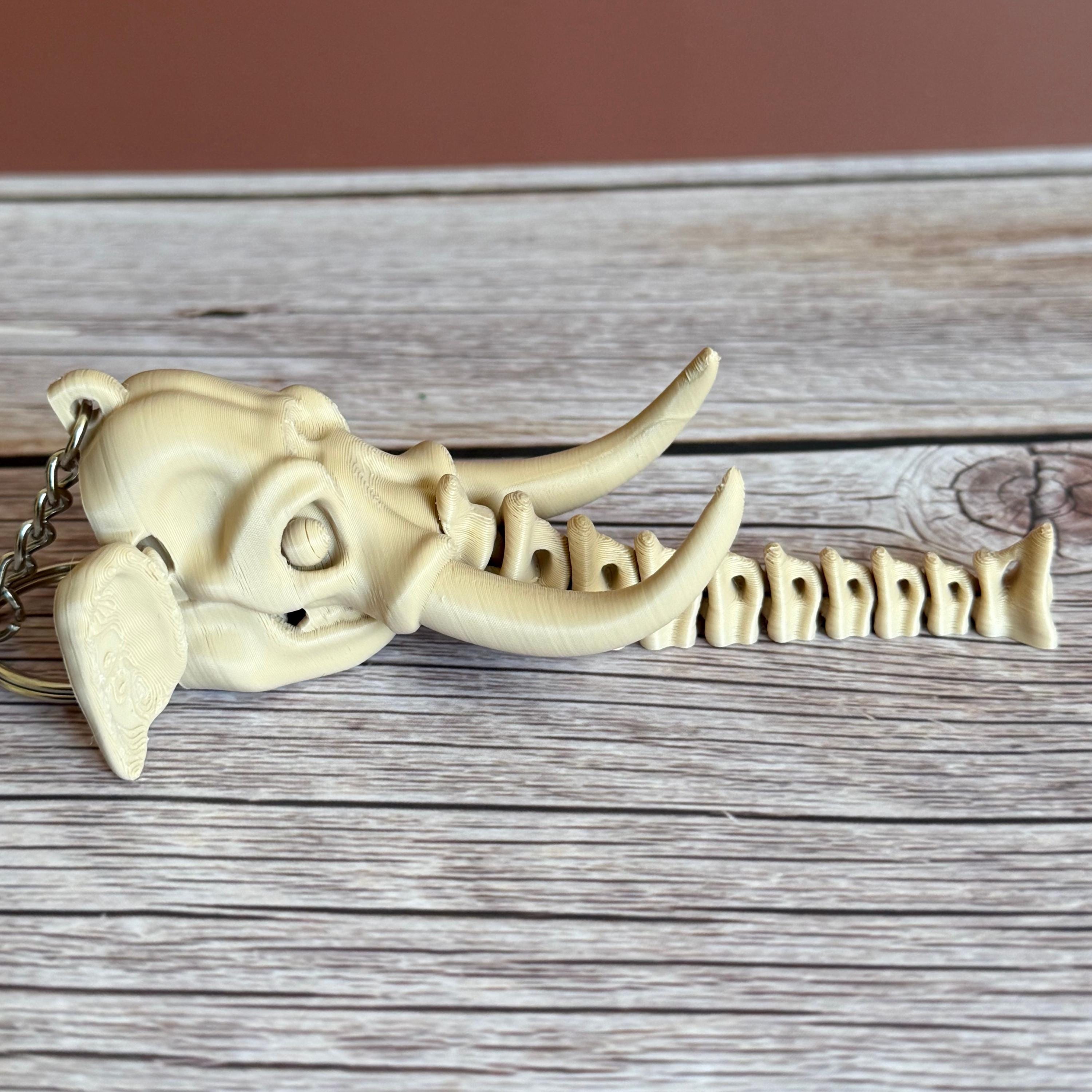 3D printed beige elephant skull with articulated skeleton-like trunk, placed on a wooden surface against a brown background