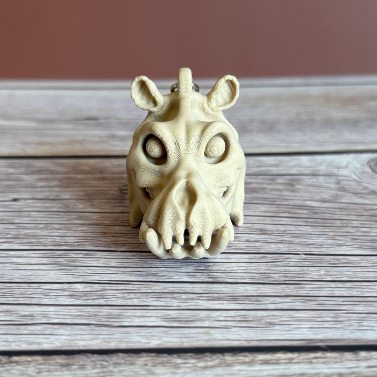 3D printed beige hippo skull keychain, placed on a wooden surface with a brown background