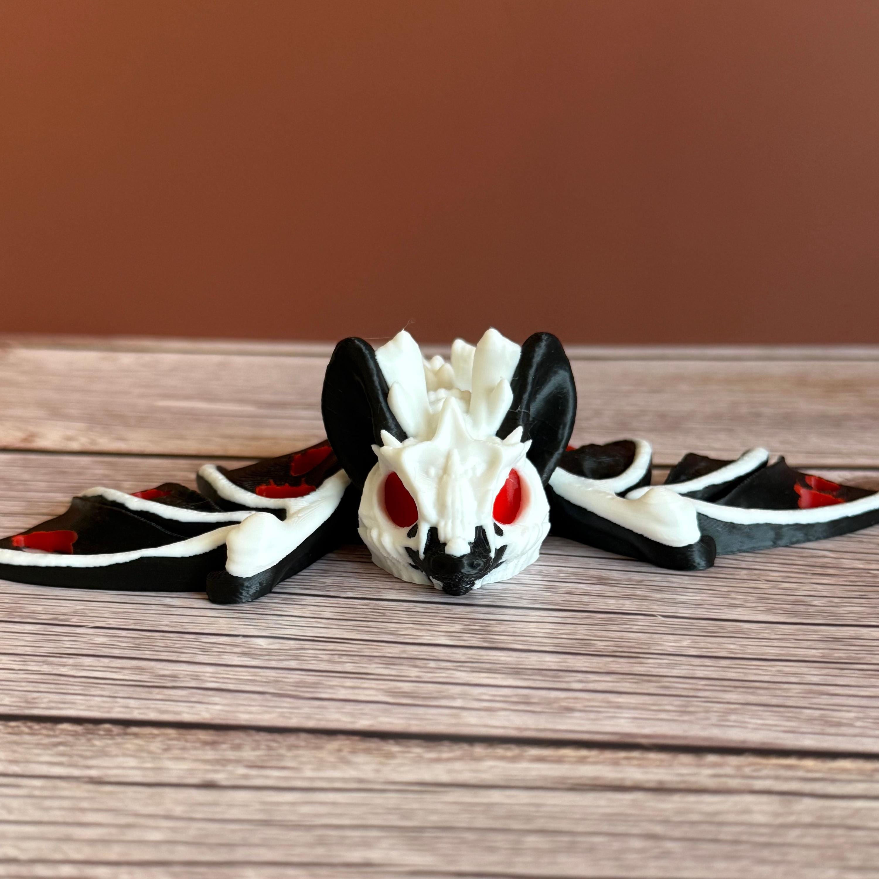 3D printed skeleton-like bat with bloody appearing wings and red eyes, placed on a wooden surface and brown background