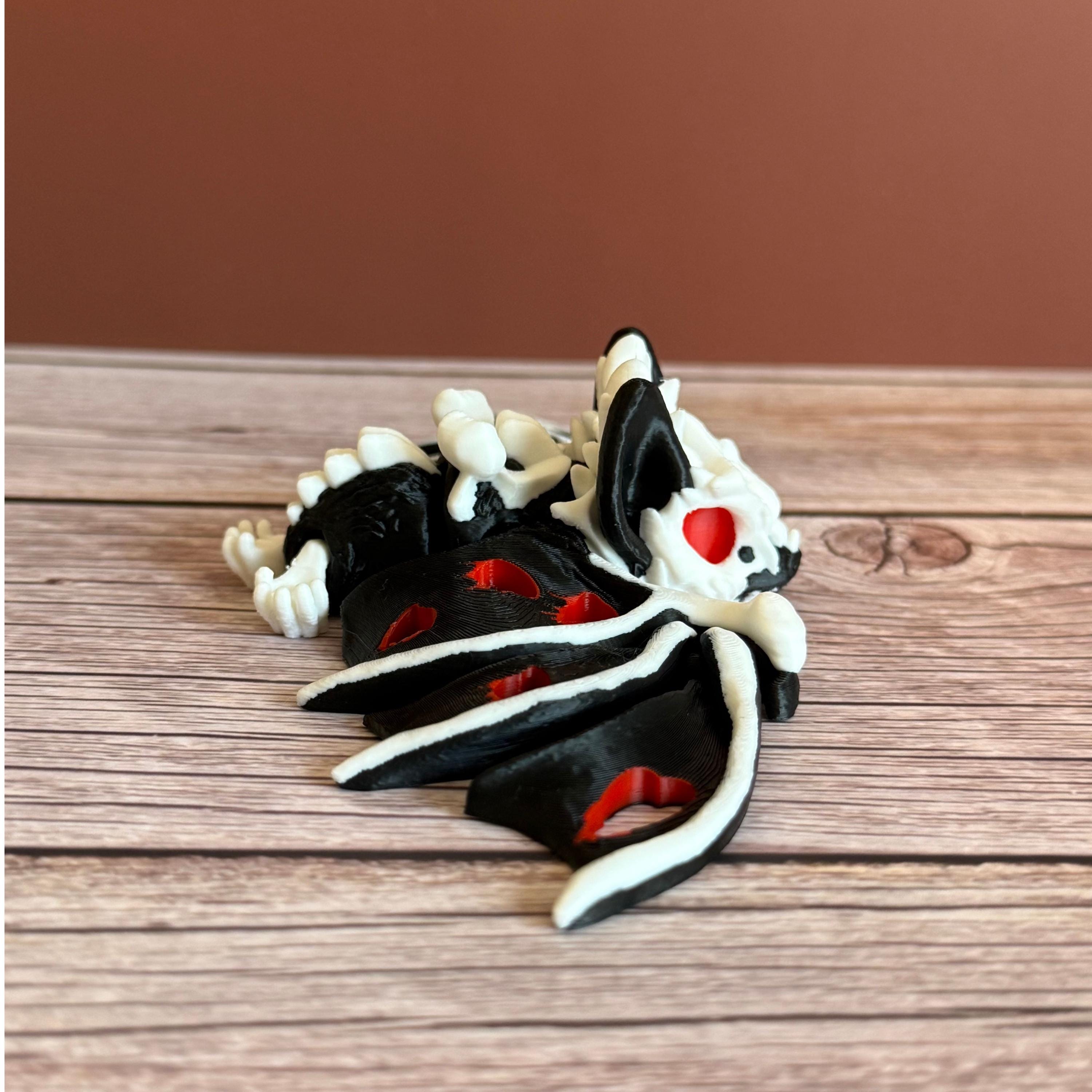 Side of a 3D printed skeleton-like bat with bloody appearing wings and red eyes, placed on a wooden surface and brown background