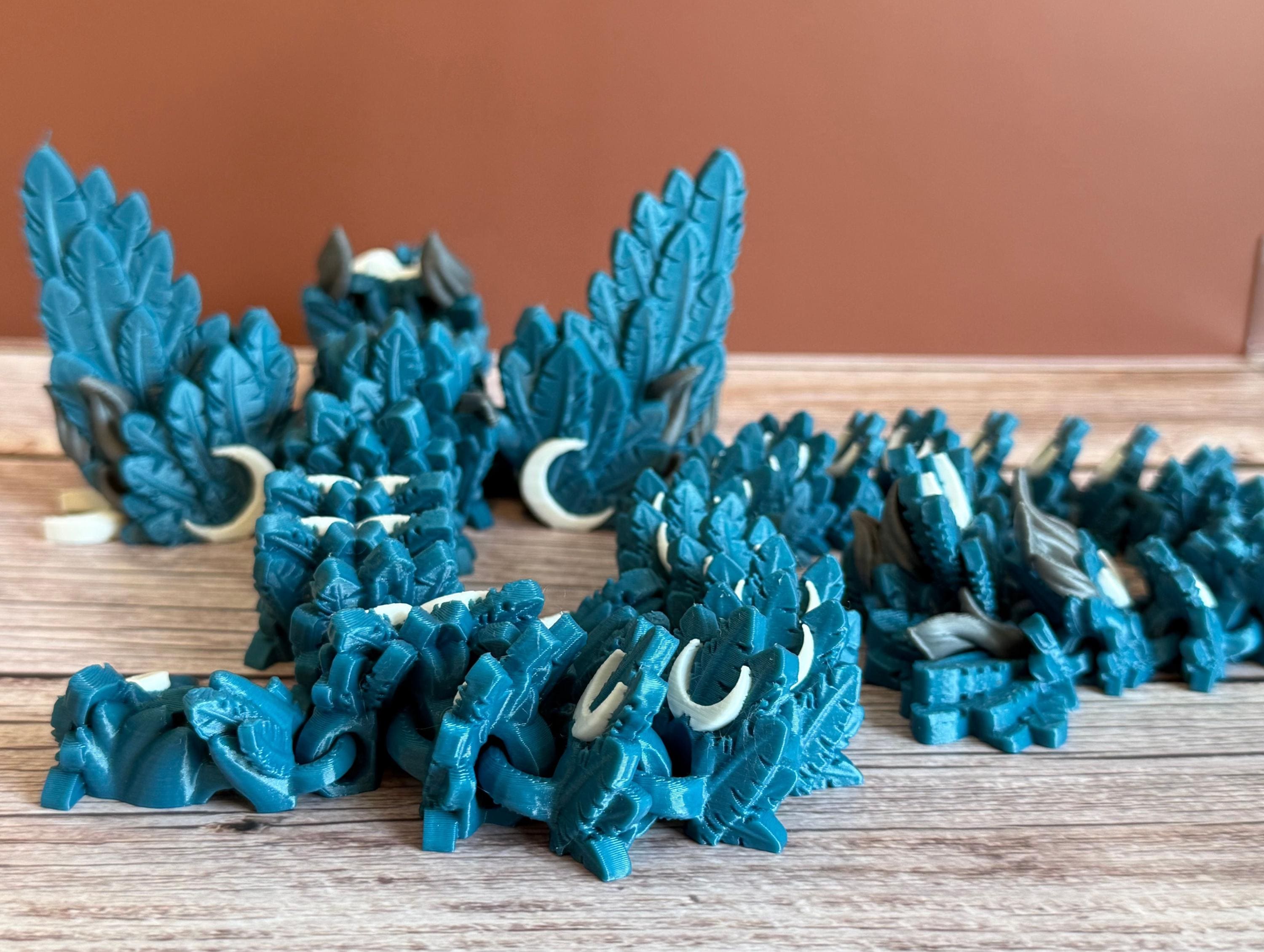 Back of a 3D printed, blue articulated dragon toy with white celestial-inspired patterns, placed on a wooden surface