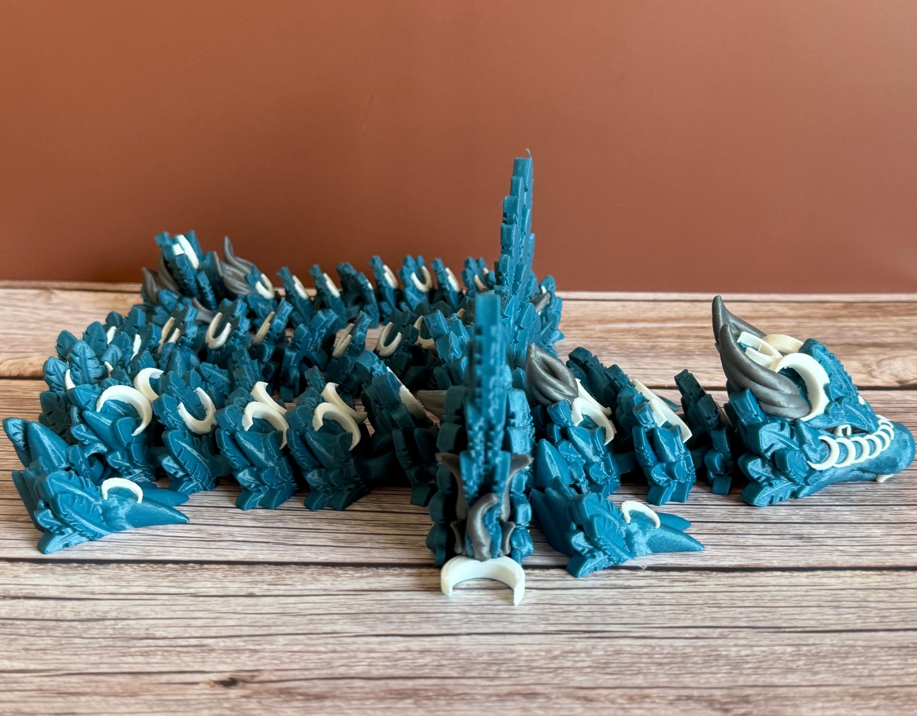 Side of a 3D printed, blue articulated dragon toy with white celestial-inspired patterns, placed on a wooden surface
