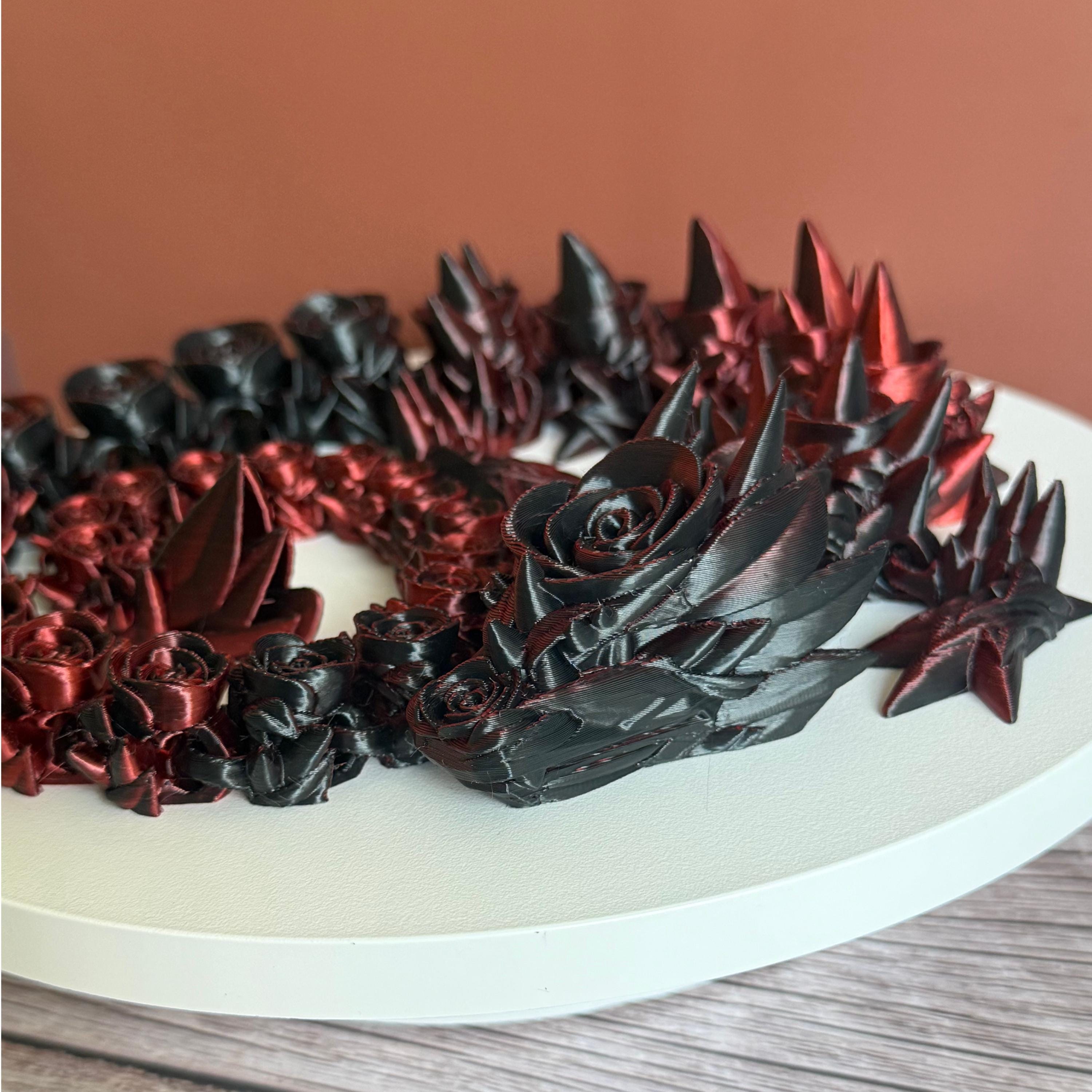 Top of 3D printed red and black dragon with rose and spike design on a white surface