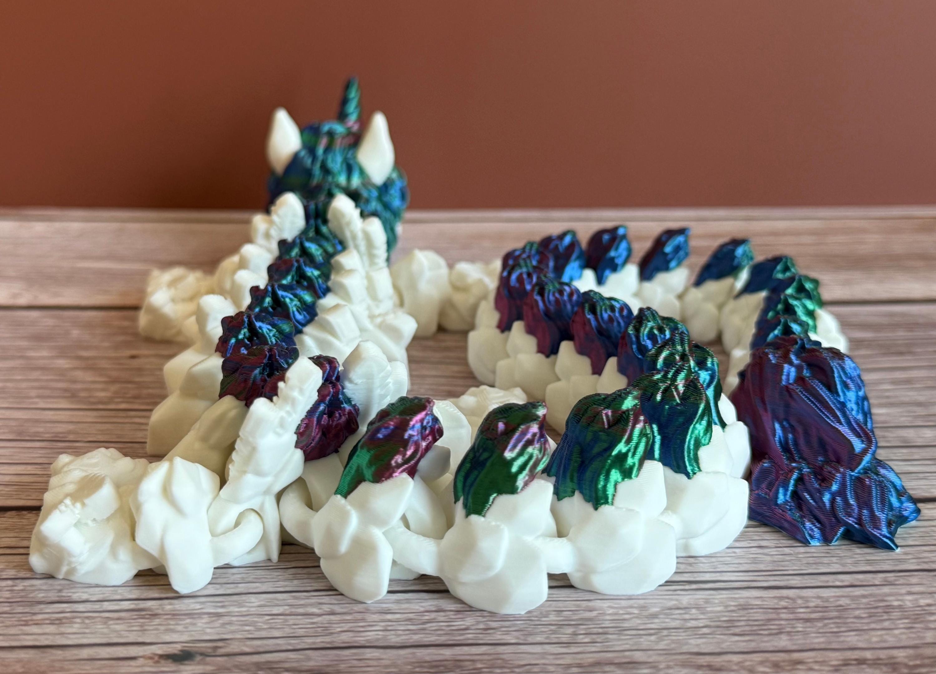Back of a 3D printed white unicorn themed dragon with multicolored mane running the length of the dragon, placed on a wooden surface