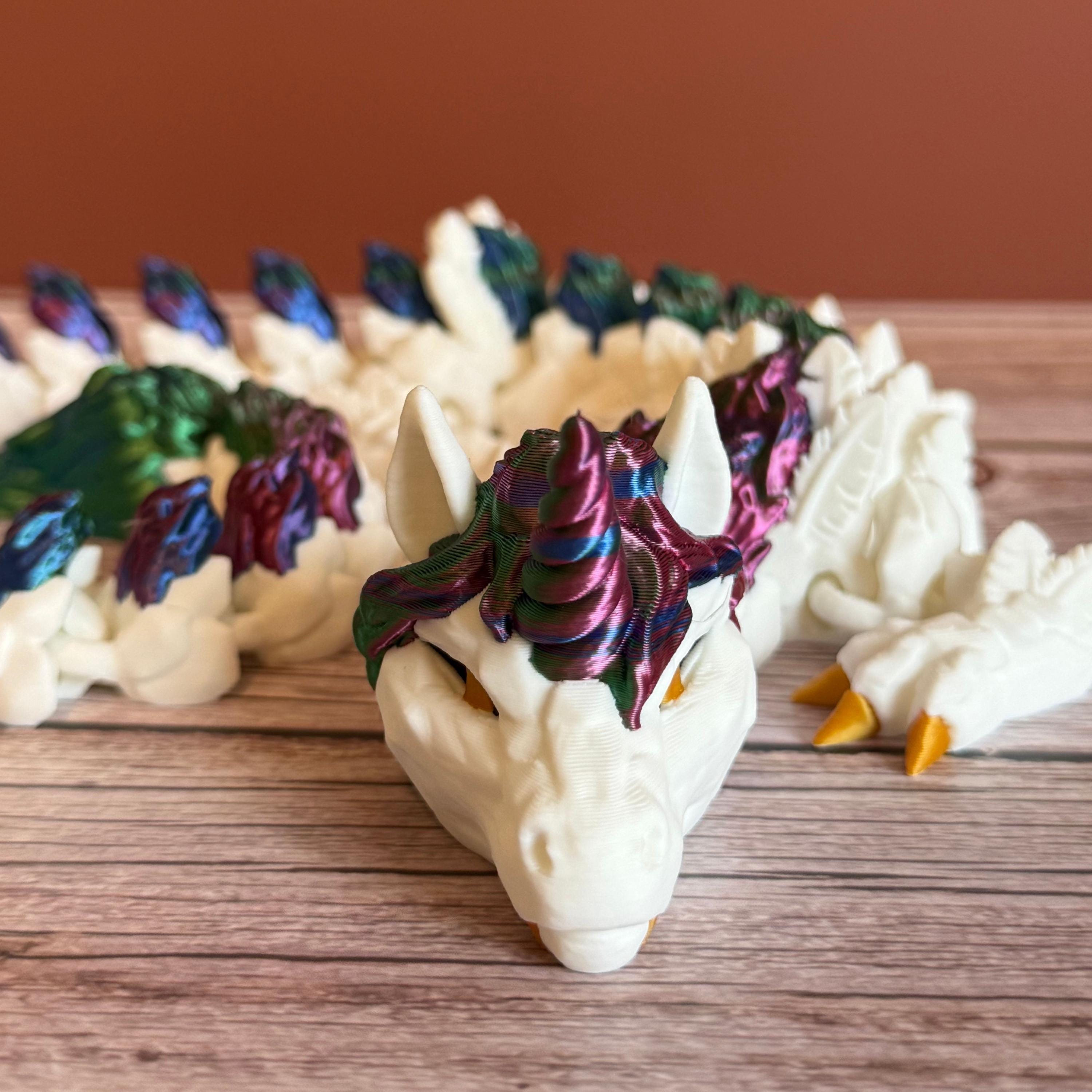 3D printed white unicorn themed dragon with multicolored mane running the length of the dragon, placed on a wooden surface